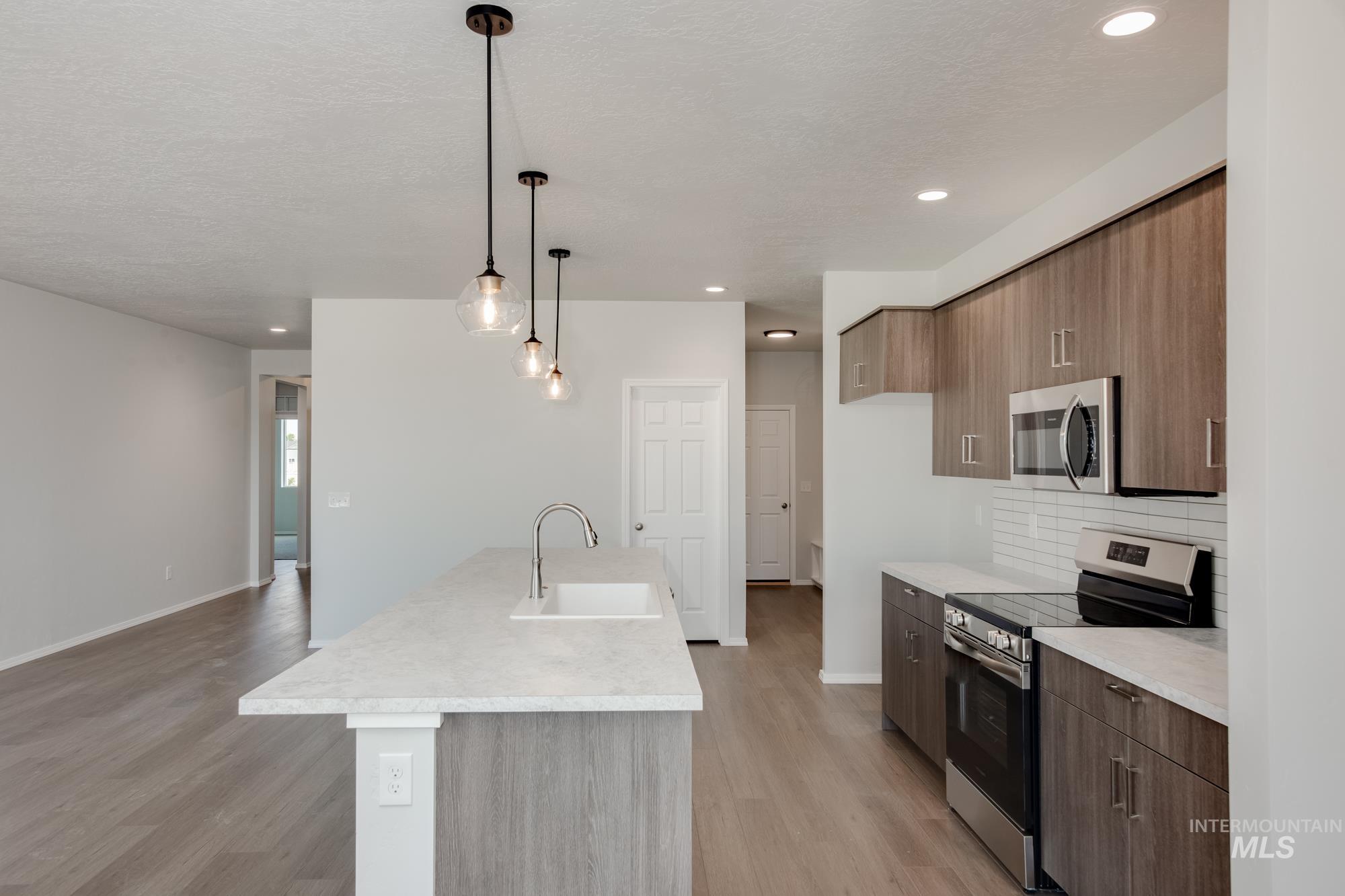 Kitchen with stainless steel appliances, modern cabinets, light countertops, decorative light fixtures, and recessed lighting