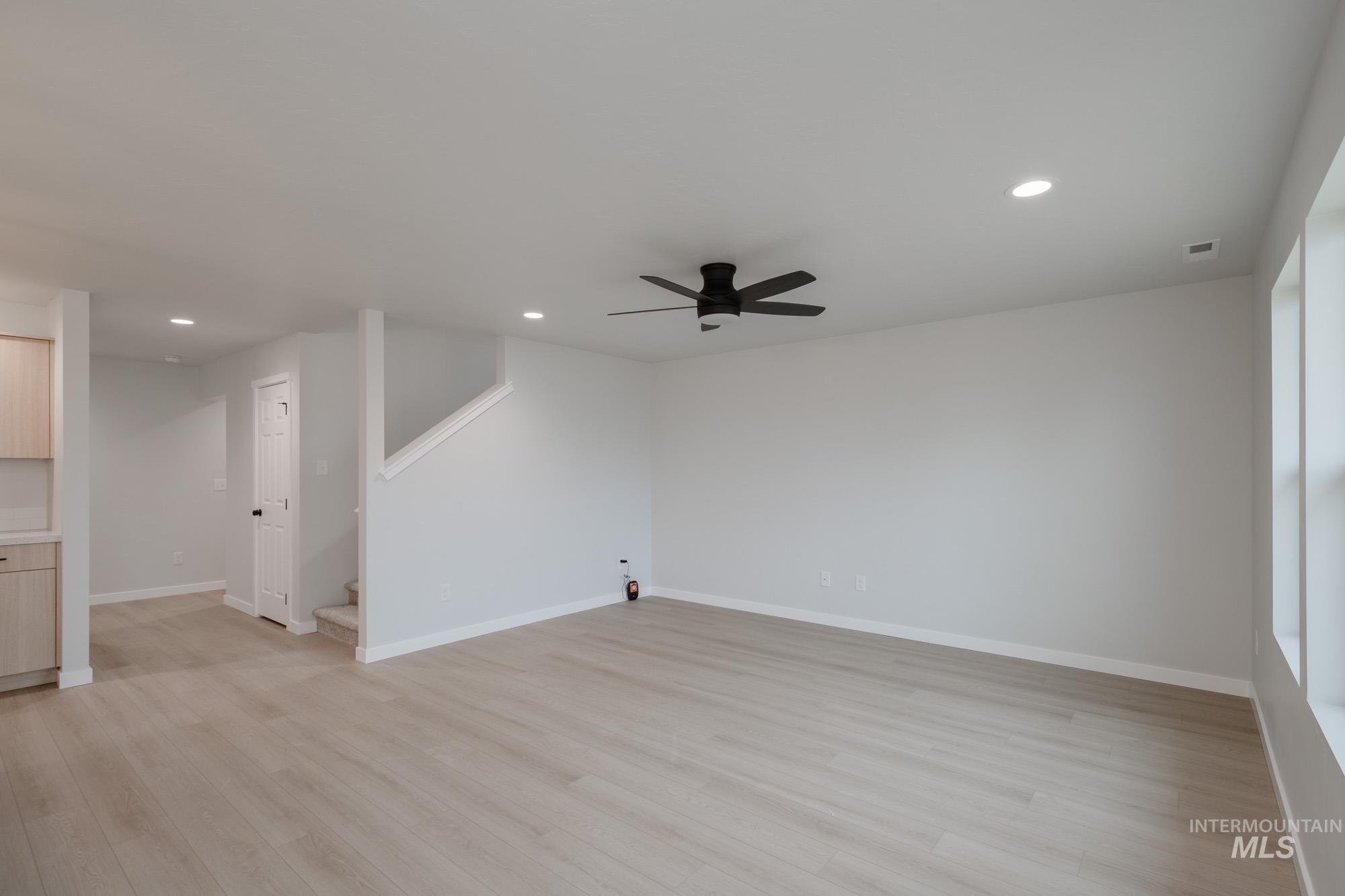Unfurnished living room with light wood-style floors, ceiling fan, recessed lighting, and stairs