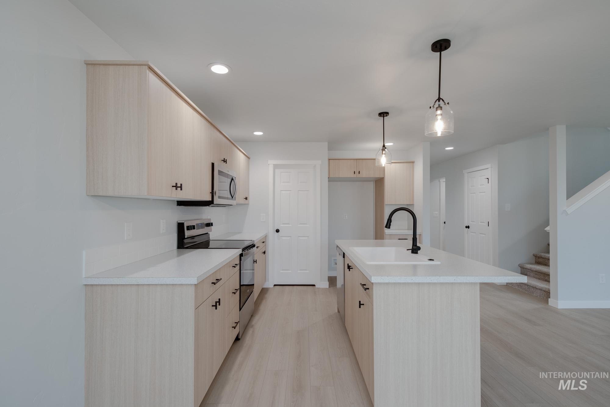 Kitchen with light brown cabinets, appliances with stainless steel finishes, light countertops, hanging light fixtures, and recessed lighting