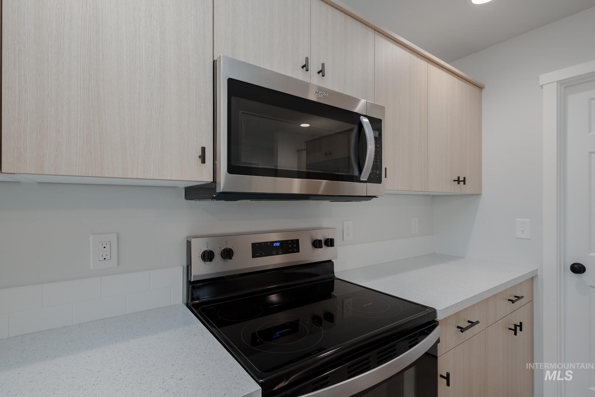 Kitchen with light brown cabinets, stainless steel appliances, light stone counters, and modern cabinets