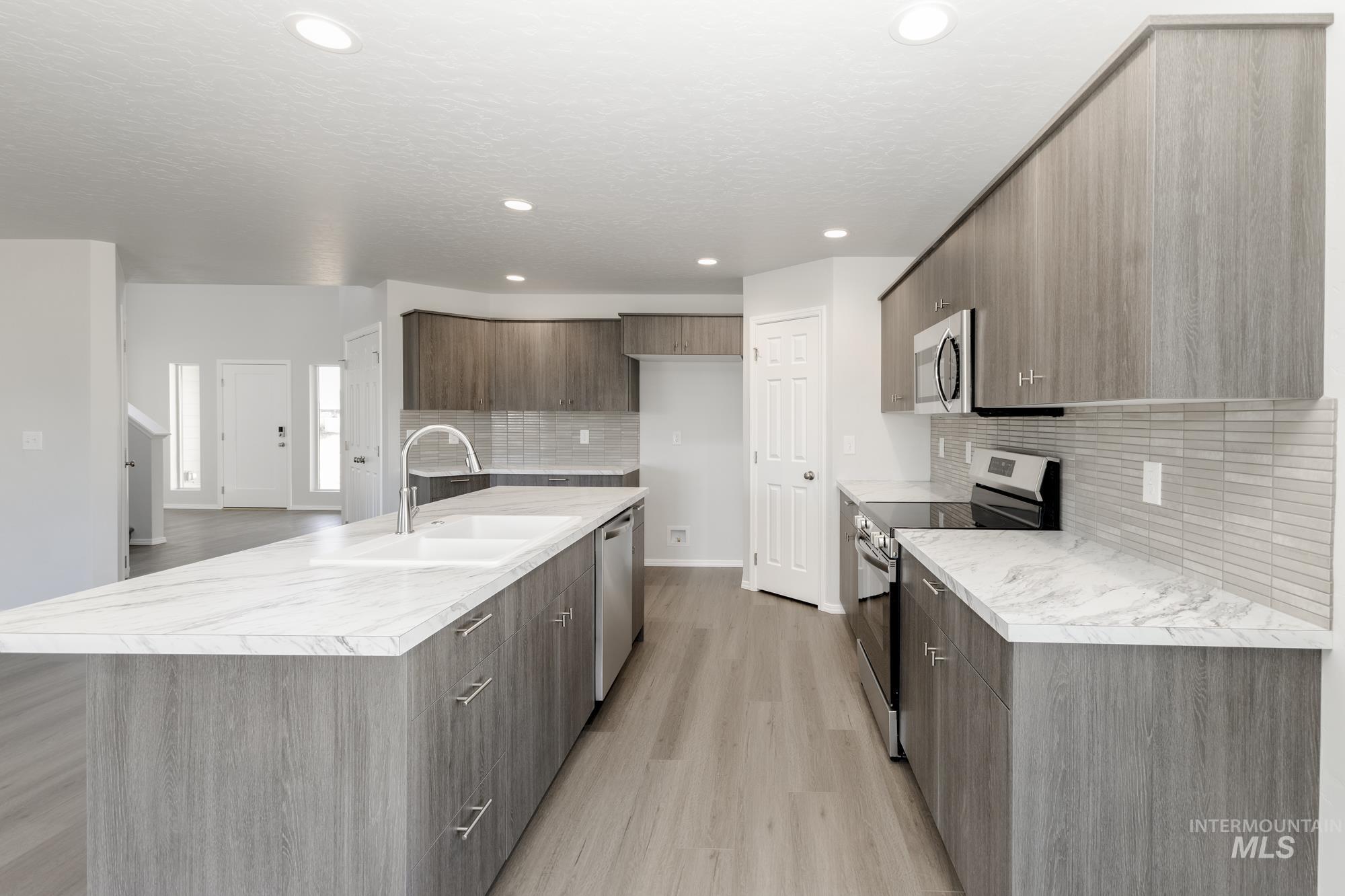 Kitchen with light countertops, stainless steel appliances, modern cabinets, a kitchen island with sink, and recessed lighting