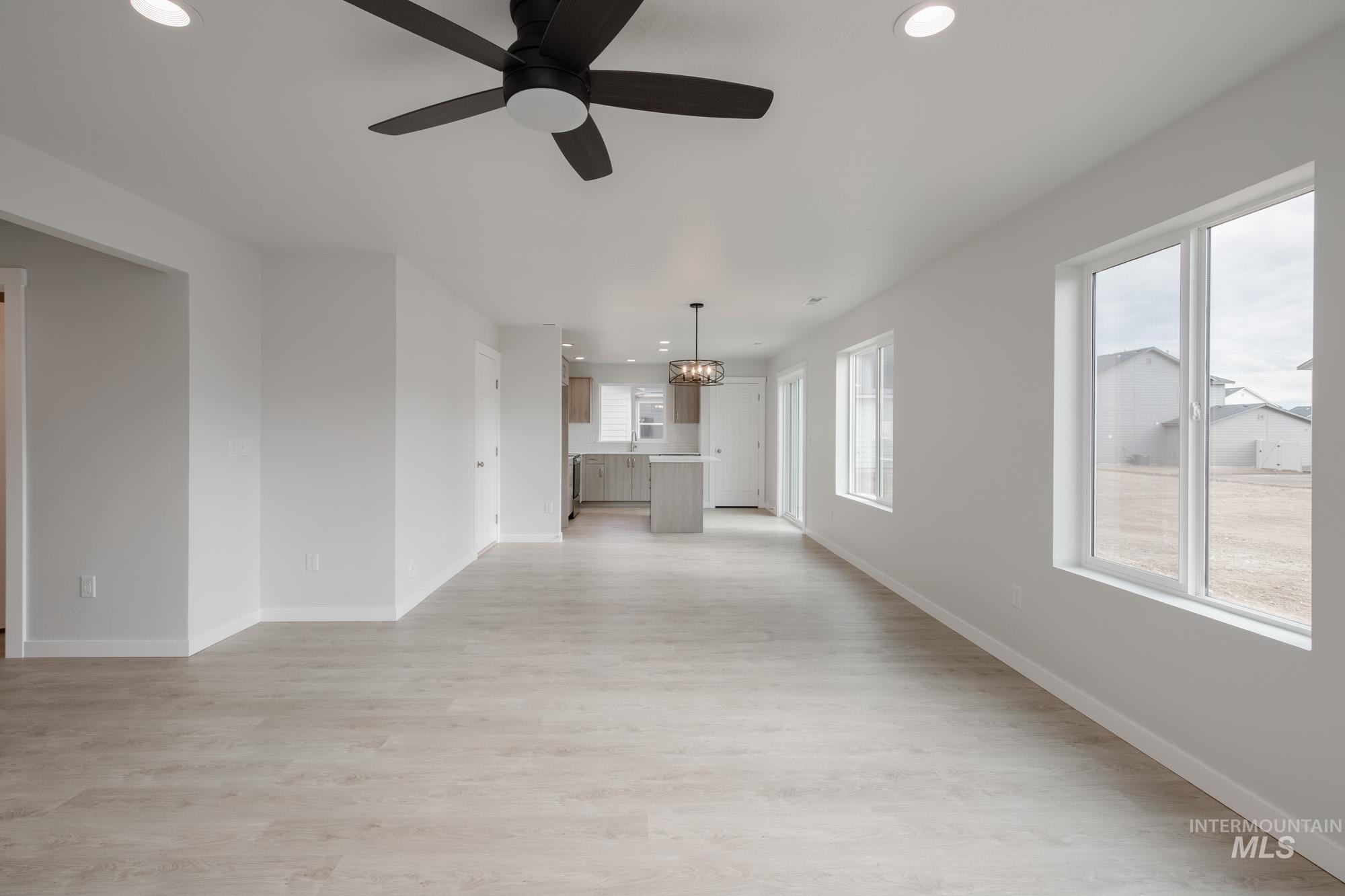 Unfurnished living room with recessed lighting, light wood-style flooring, ceiling fan, and a chandelier