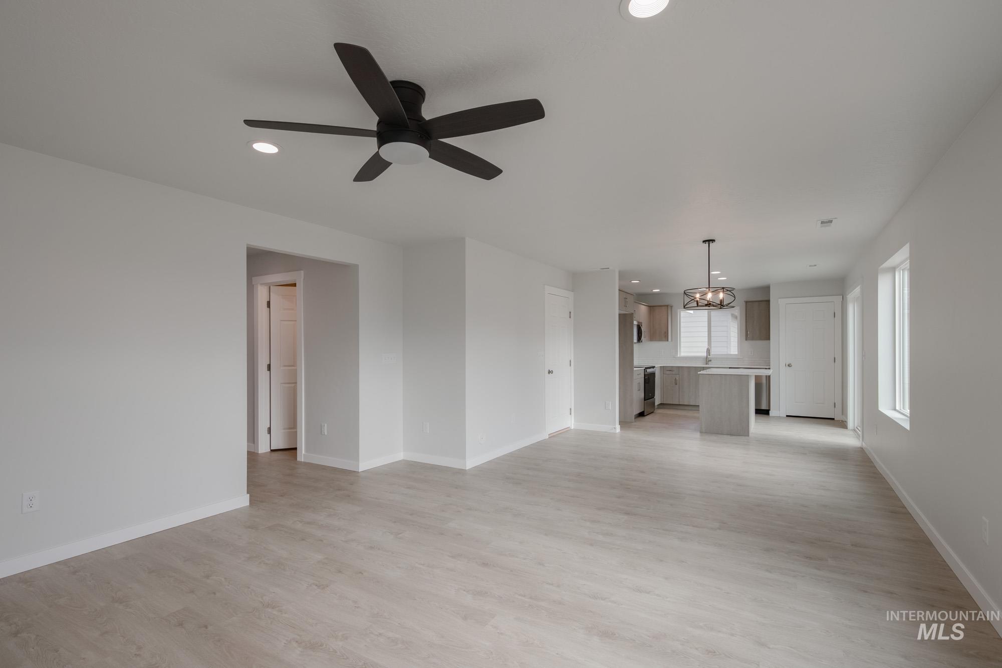 Unfurnished living room with light wood finished floors, recessed lighting, ceiling fan, and a chandelier