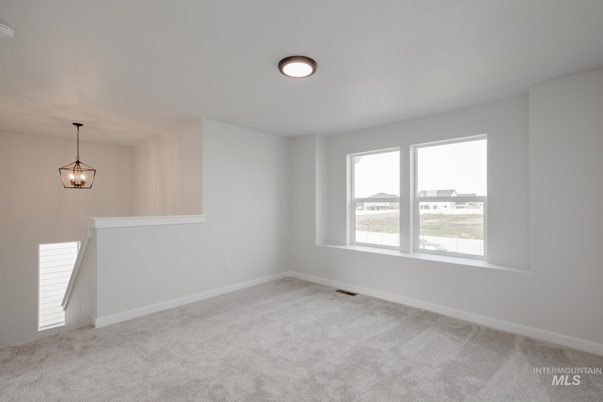 Spare room featuring light colored carpet and a chandelier