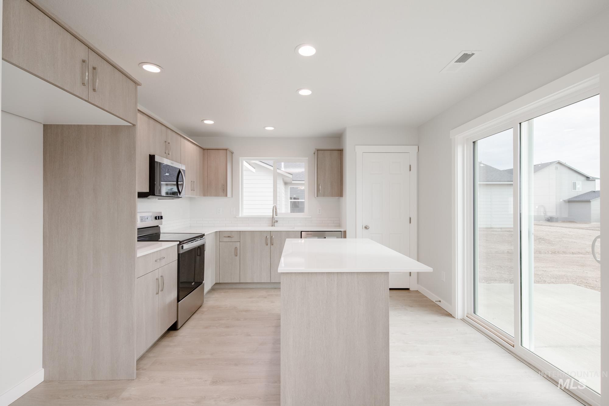 Kitchen with light brown cabinetry, stainless steel appliances, a kitchen island, modern cabinets, and recessed lighting