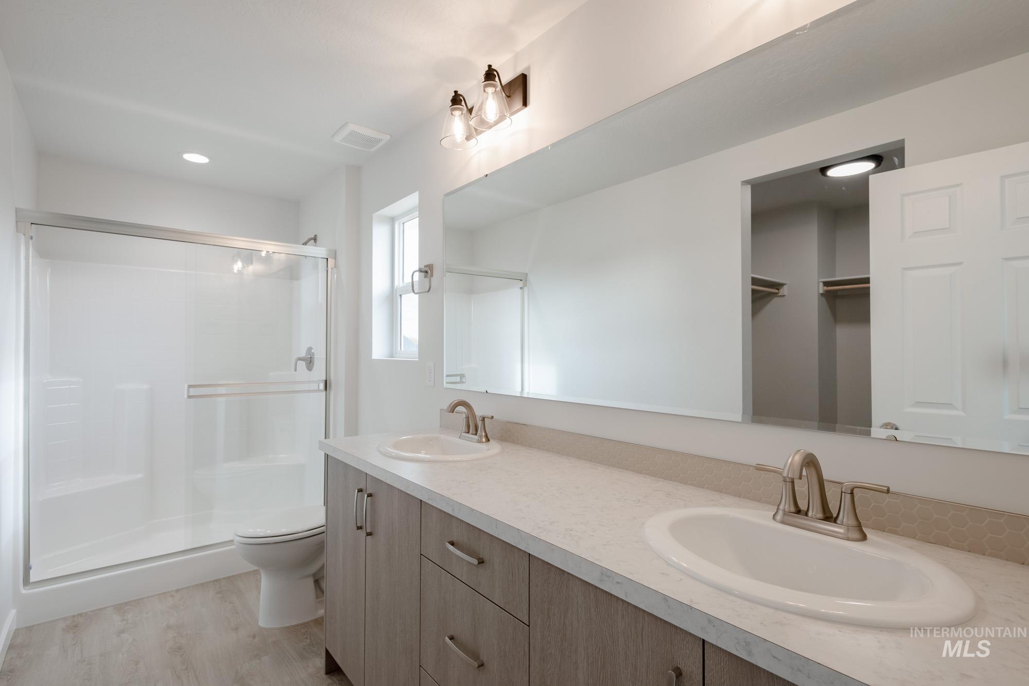 Full bath with double vanity, a stall shower, light wood-style flooring, and recessed lighting