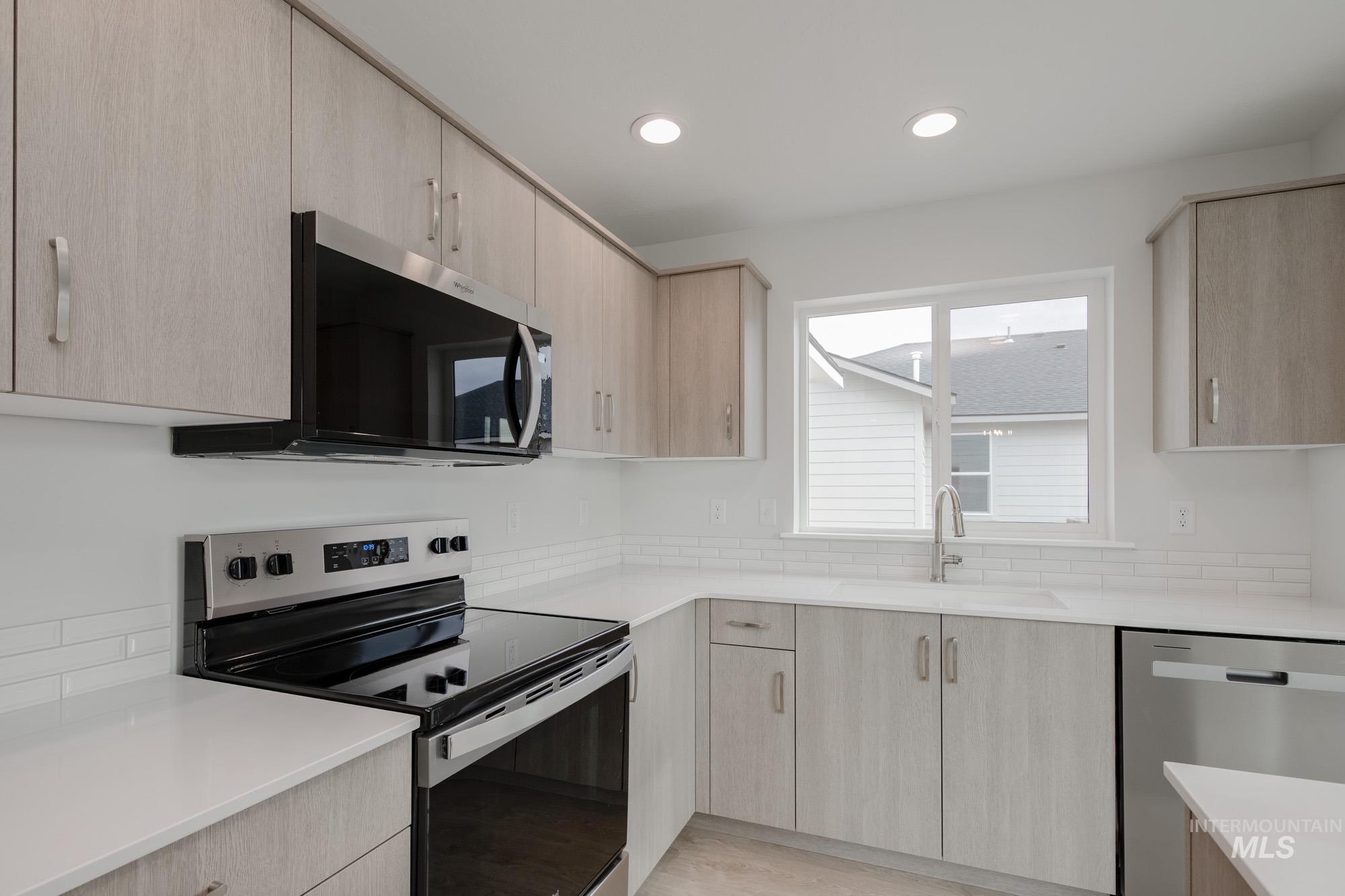 Kitchen with light brown cabinets, appliances with stainless steel finishes, light stone counters, modern cabinets, and recessed lighting