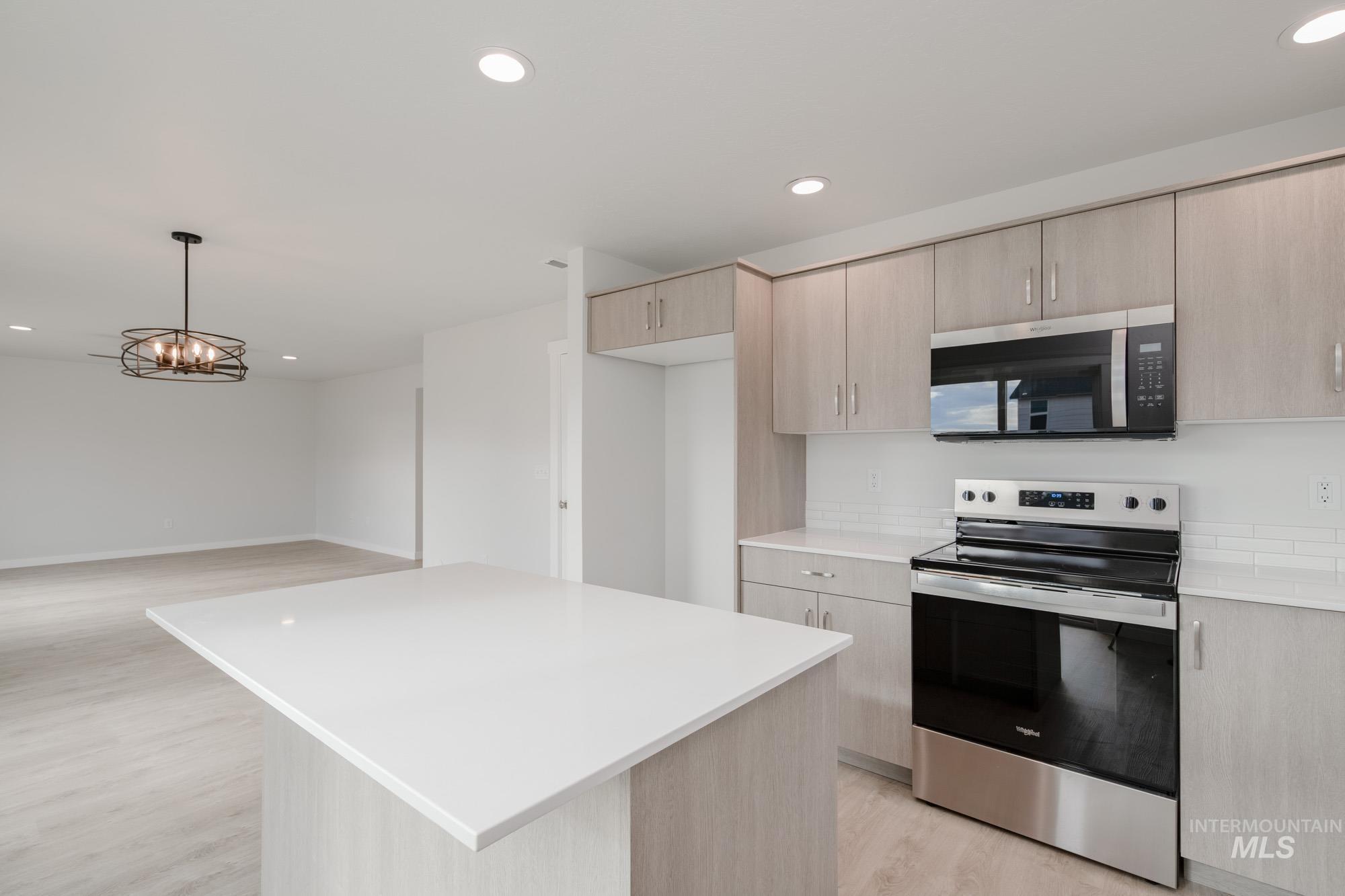 Kitchen with light brown cabinetry, stainless steel appliances, a center island, recessed lighting, and decorative light fixtures