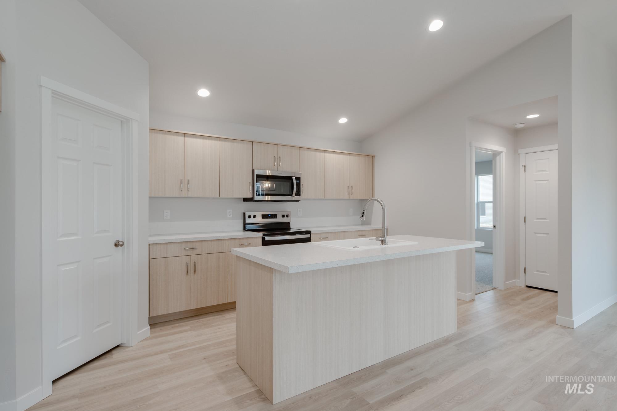 Kitchen with light countertops, an island with sink, light brown cabinets, appliances with stainless steel finishes, and light wood-style flooring