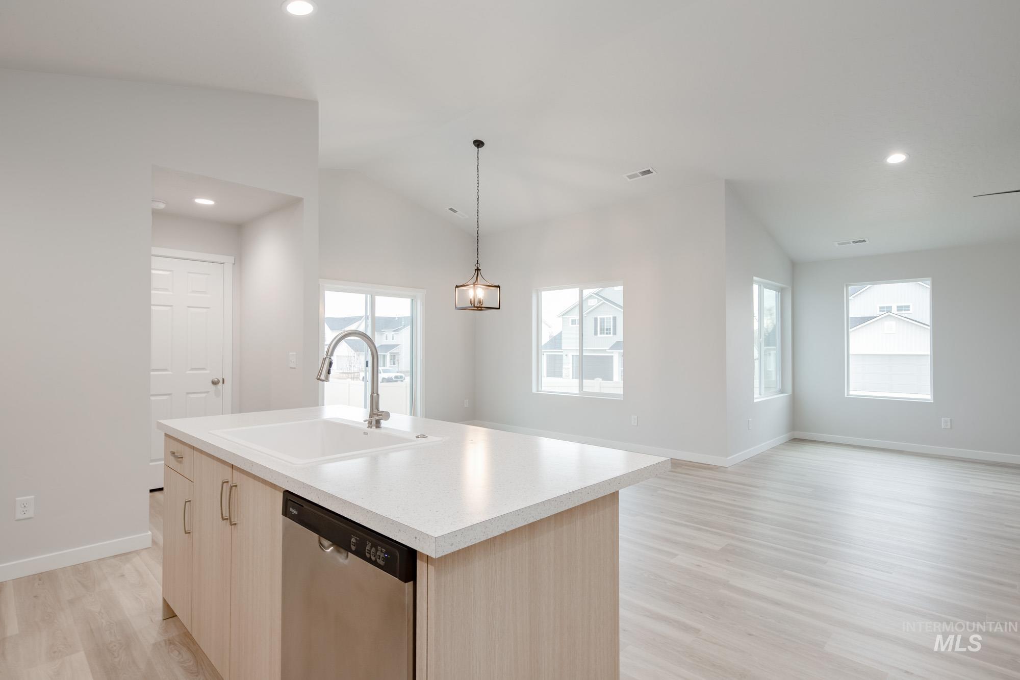 Kitchen featuring light brown cabinetry, vaulted ceiling, light countertops, stainless steel dishwasher, and light wood-style floors