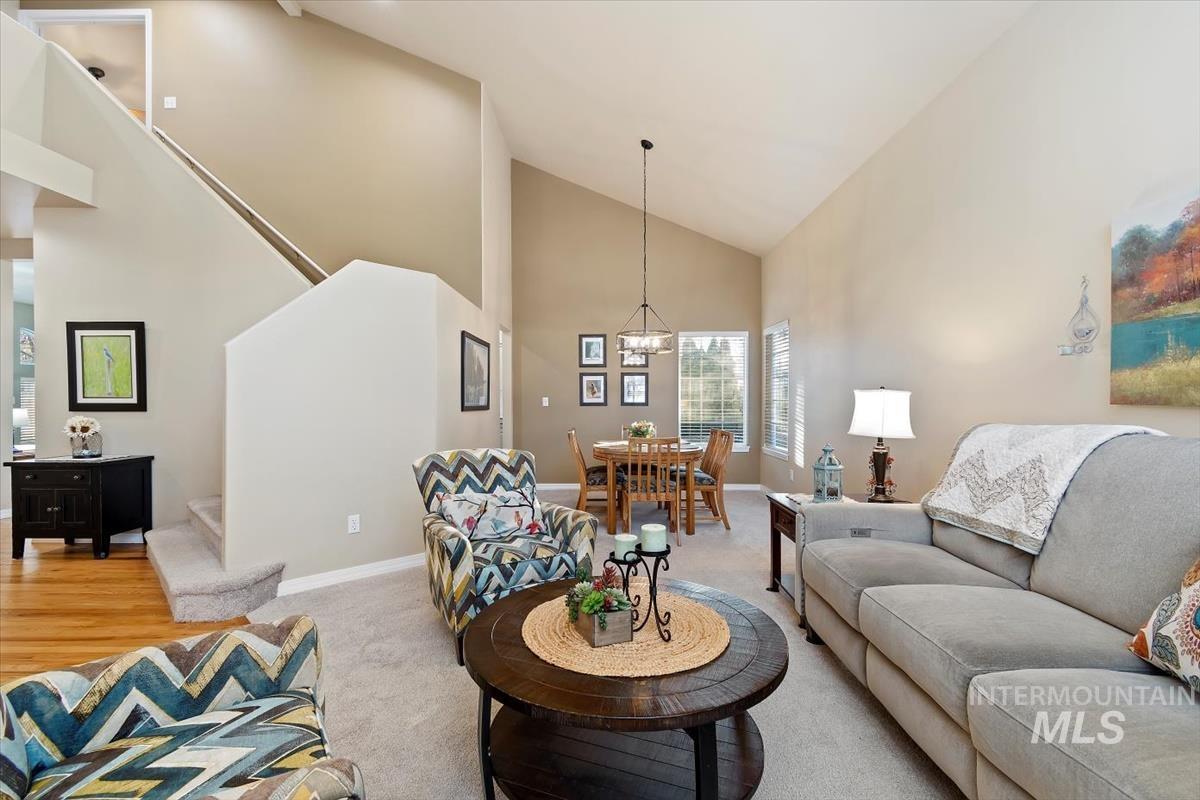 Carpeted living room with high vaulted ceiling, stairway, and a chandelier