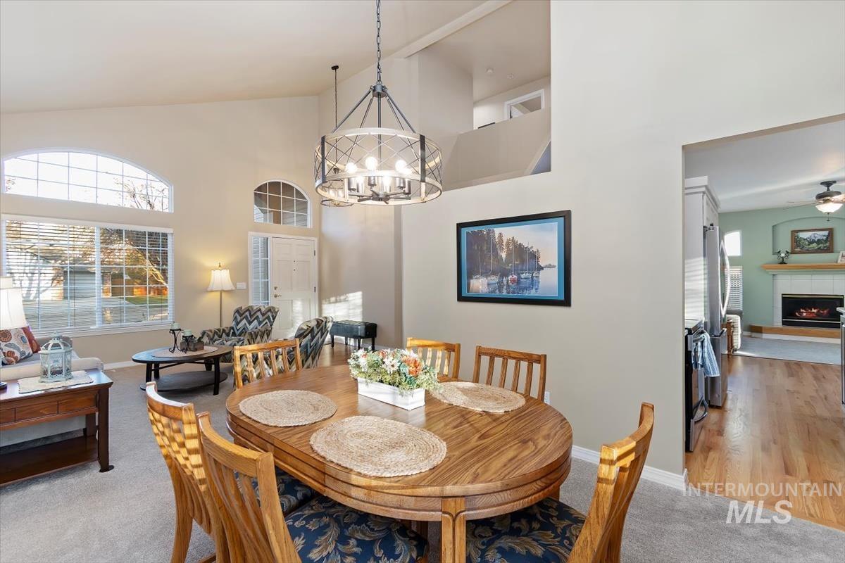 Dining room featuring light colored carpet, a fireplace, high vaulted ceiling, plenty of natural light, and a chandelier