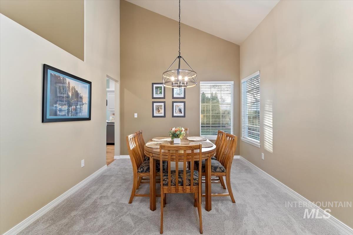 Dining space featuring high vaulted ceiling, light carpet, and a chandelier
