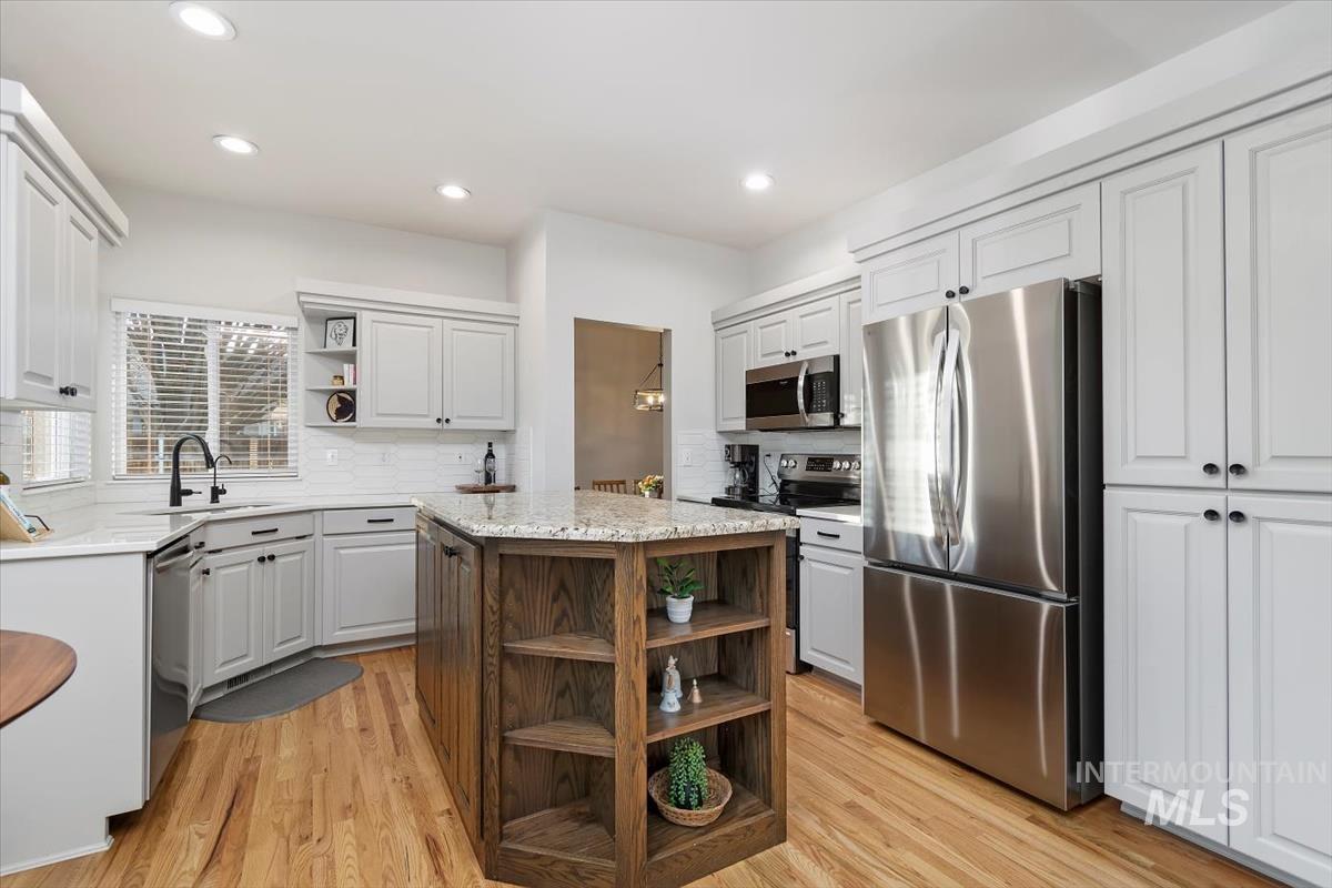 Kitchen with open shelves, stainless steel appliances, light stone counters, a kitchen island, and light wood-style flooring