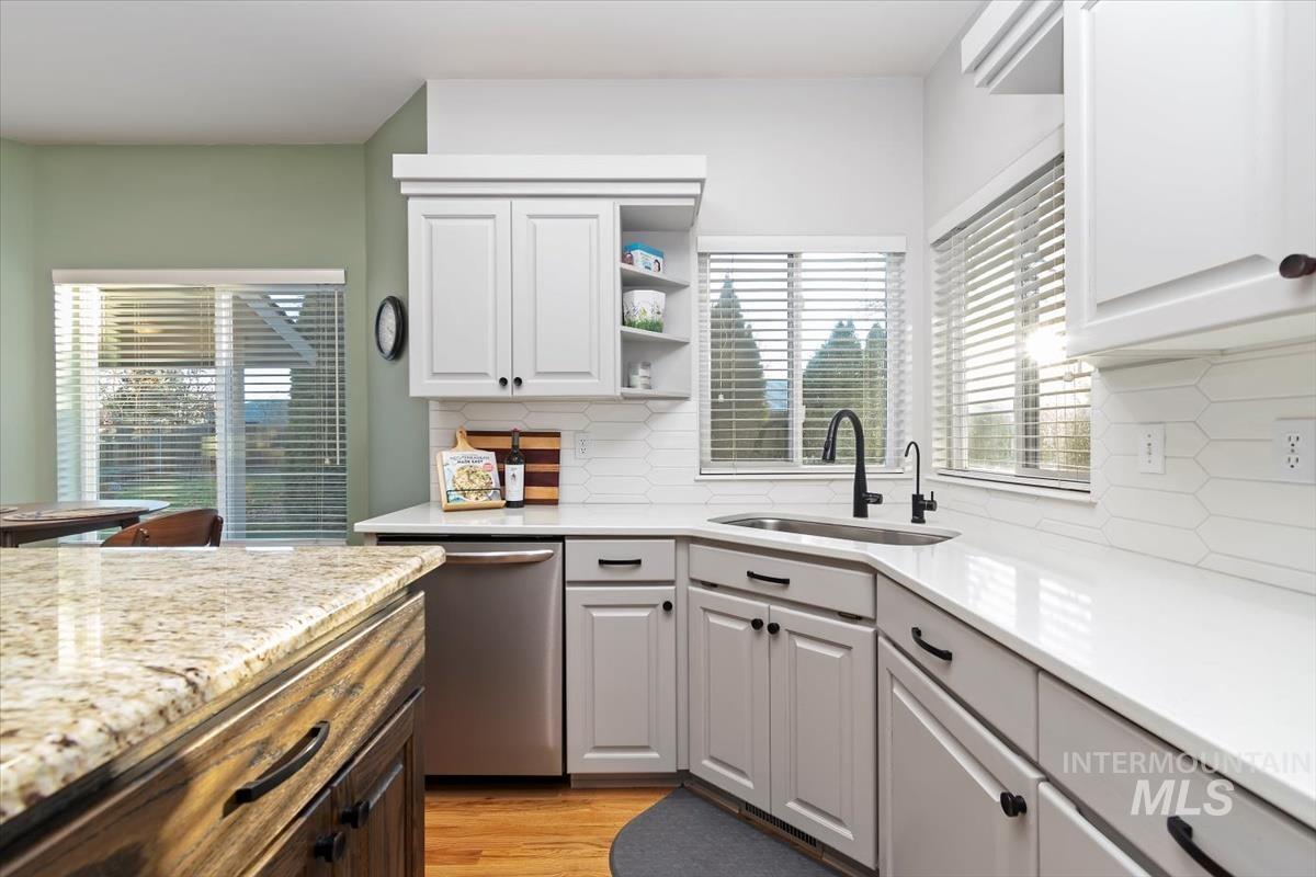 Kitchen with stainless steel dishwasher, open shelves, light stone countertops, light wood-style flooring, and white cabinets