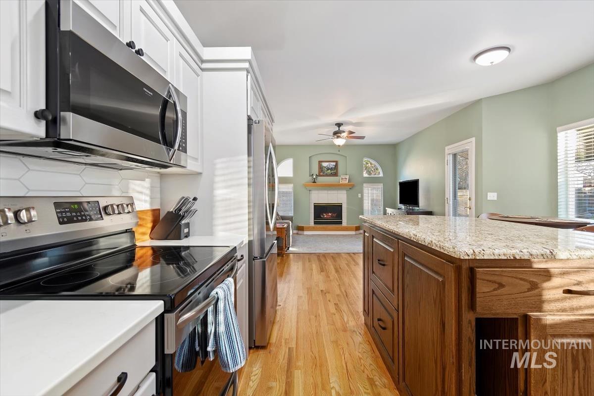Kitchen featuring appliances with stainless steel finishes, a warm lit fireplace, open floor plan, light stone countertops, and a ceiling fan