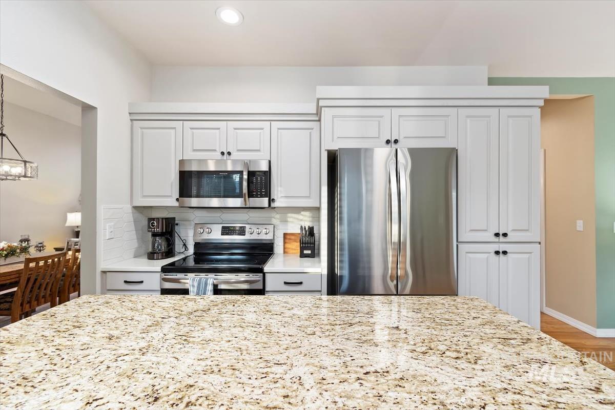 Kitchen featuring appliances with stainless steel finishes, light stone counters, backsplash, and white cabinets