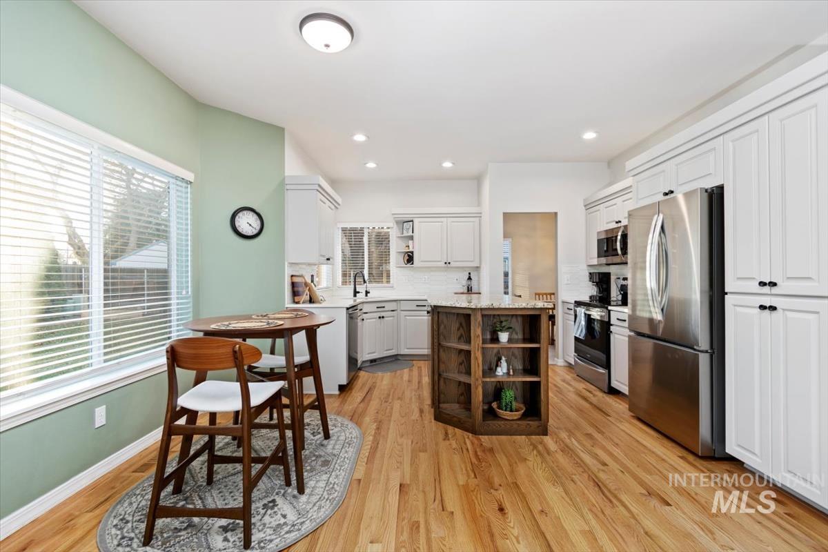 Kitchen featuring open shelves, appliances with stainless steel finishes, white cabinets, decorative backsplash, and light wood finished floors