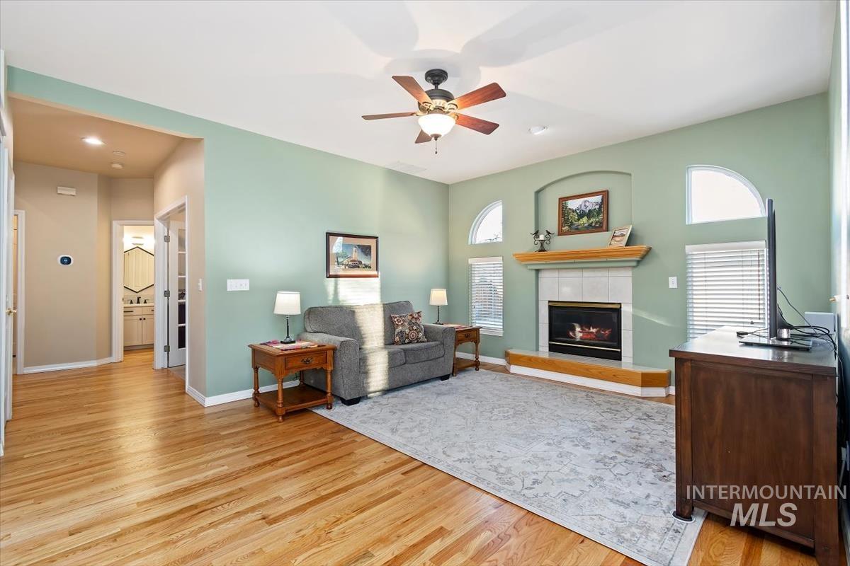 Living room with a fireplace, light wood-style flooring, and a ceiling fan