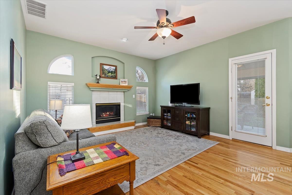 Living area featuring a tile fireplace, healthy amount of natural light, light wood-type flooring, and ceiling fan