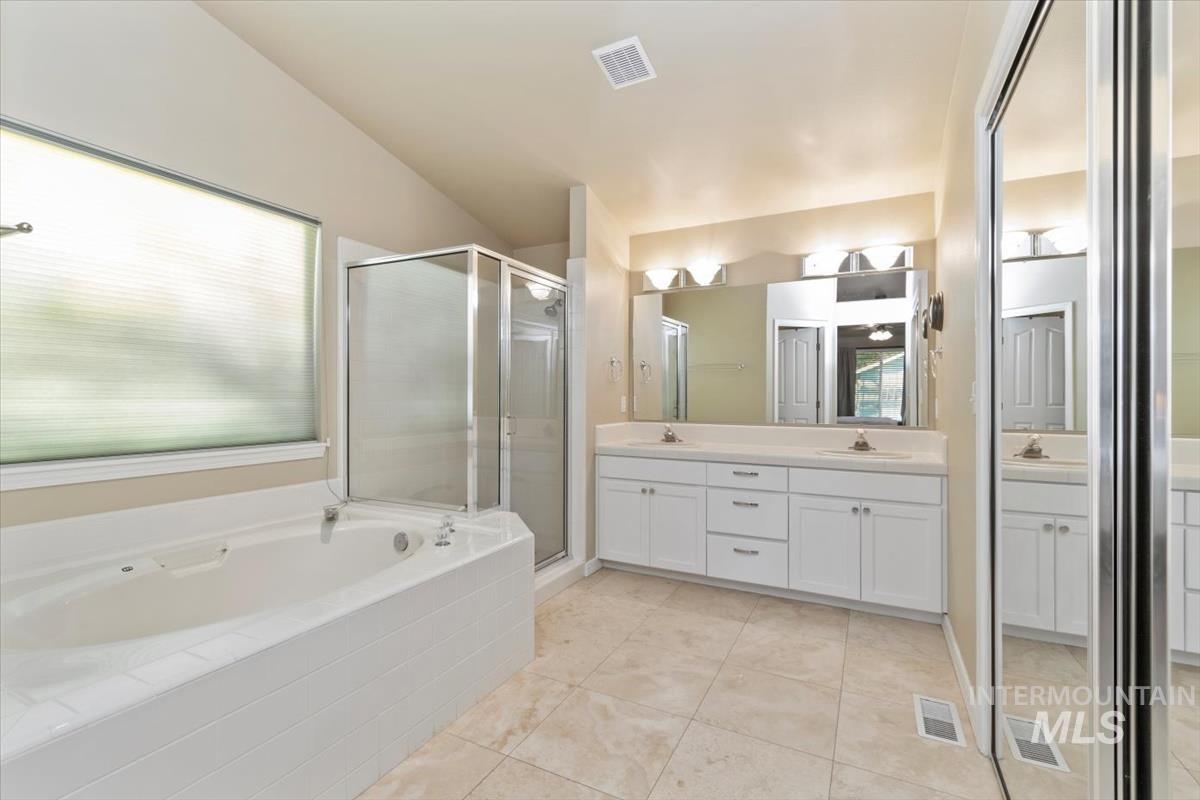 Bathroom featuring double vanity, a bath, a shower stall, light tile patterned flooring, and vaulted ceiling