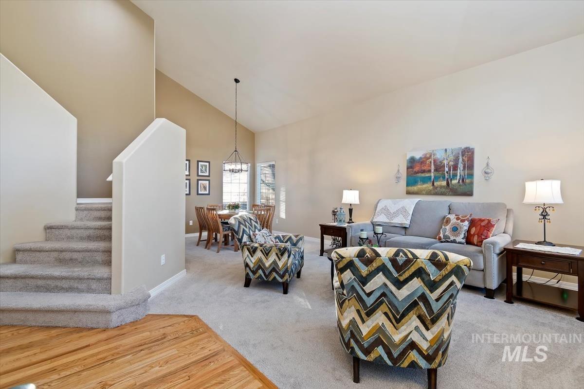 Living area featuring high vaulted ceiling, light carpet, stairs, and a chandelier