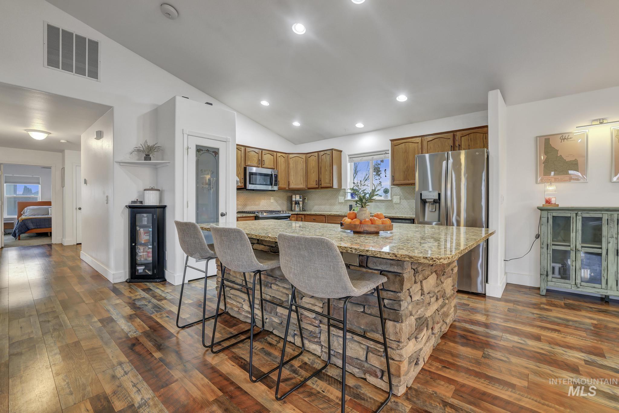 Kitchen with lofted ceiling, a kitchen island, light stone countertops, stainless steel appliances, and a kitchen breakfast bar