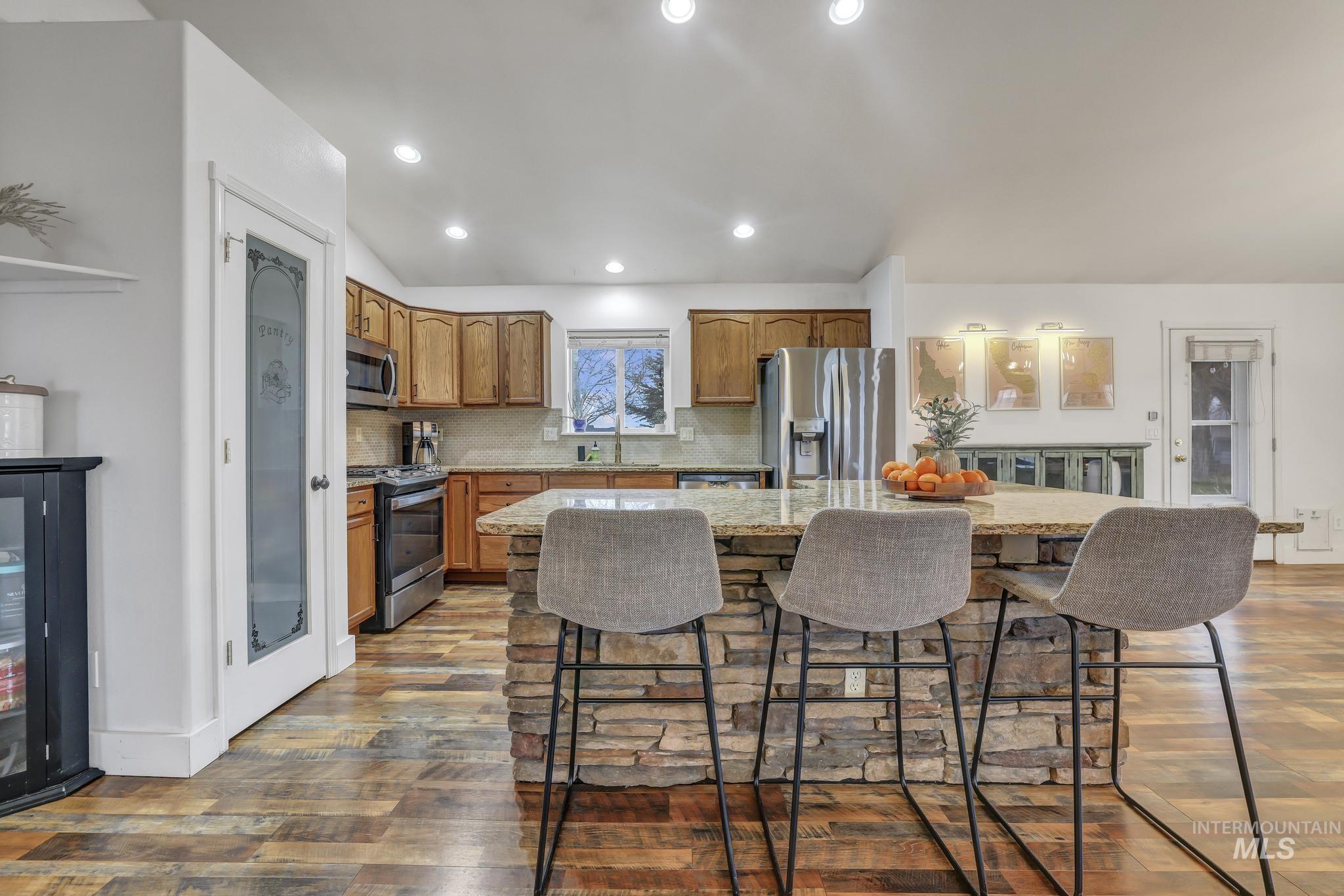 Kitchen with light stone counters, stainless steel appliances, a center island, dark wood-style floors, and brown cabinetry