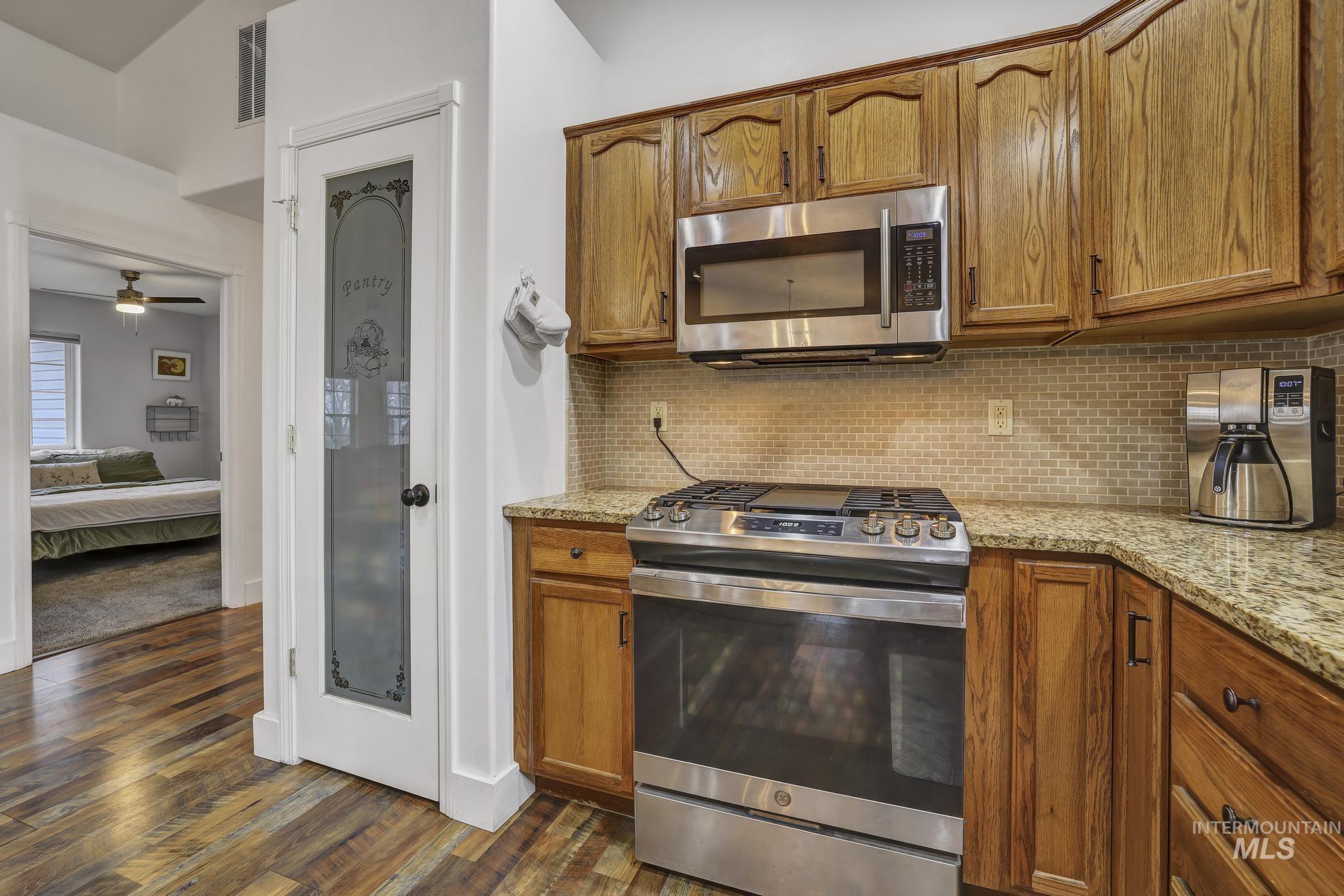 Kitchen with appliances with stainless steel finishes, brown cabinetry, and light stone countertops