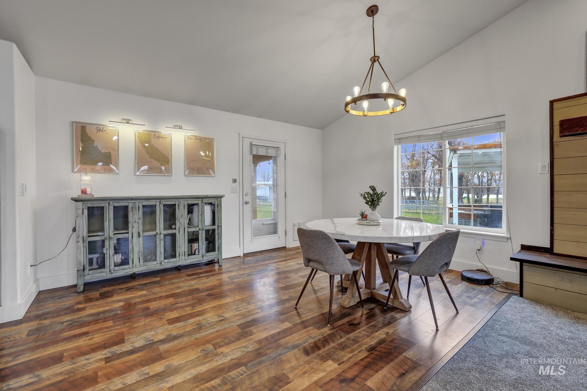 Dining room featuring healthy amount of natural light, wood-type flooring, a chandelier, and high vaulted ceiling