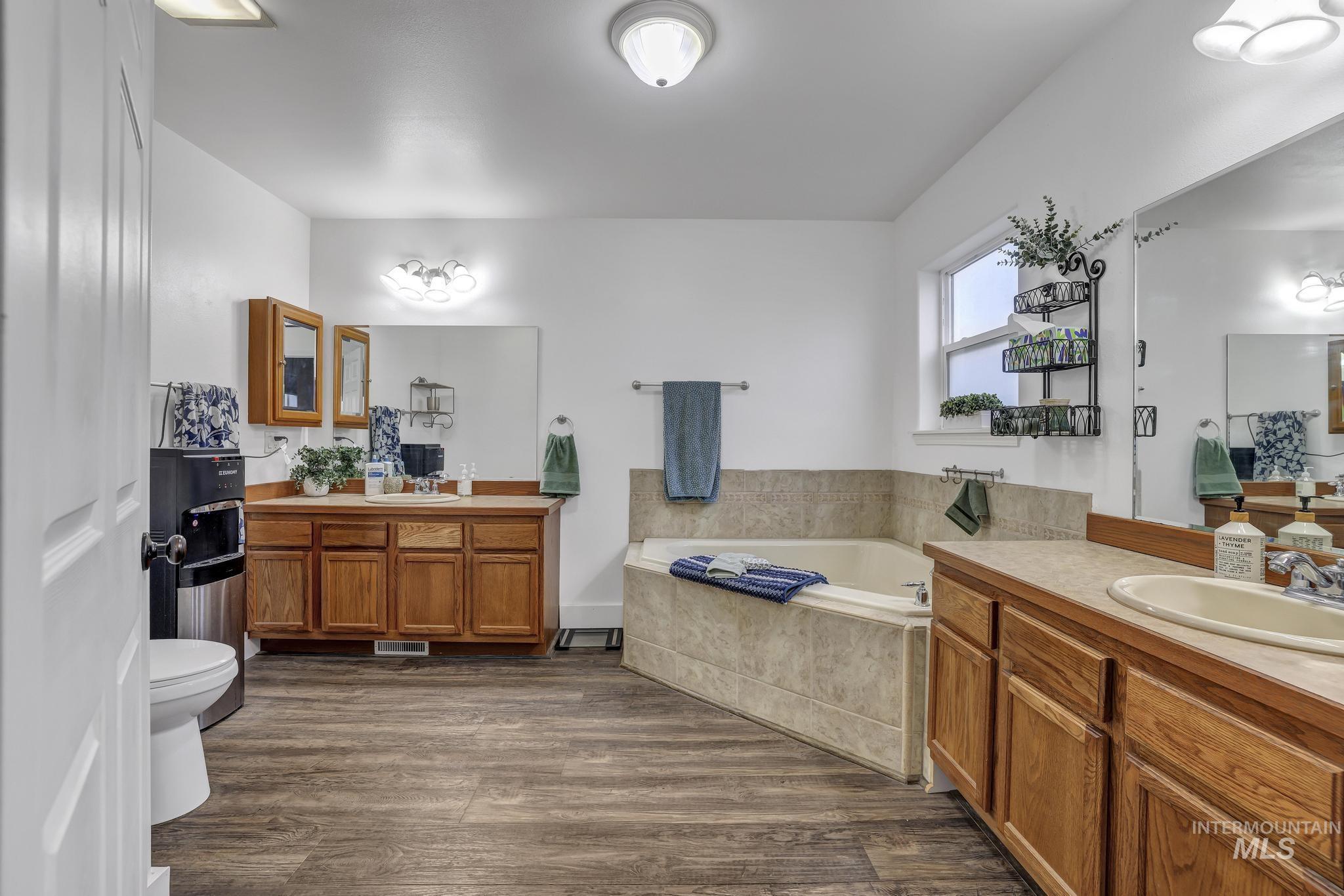 Full bathroom featuring two vanities, dark wood-style floors, and a garden tub