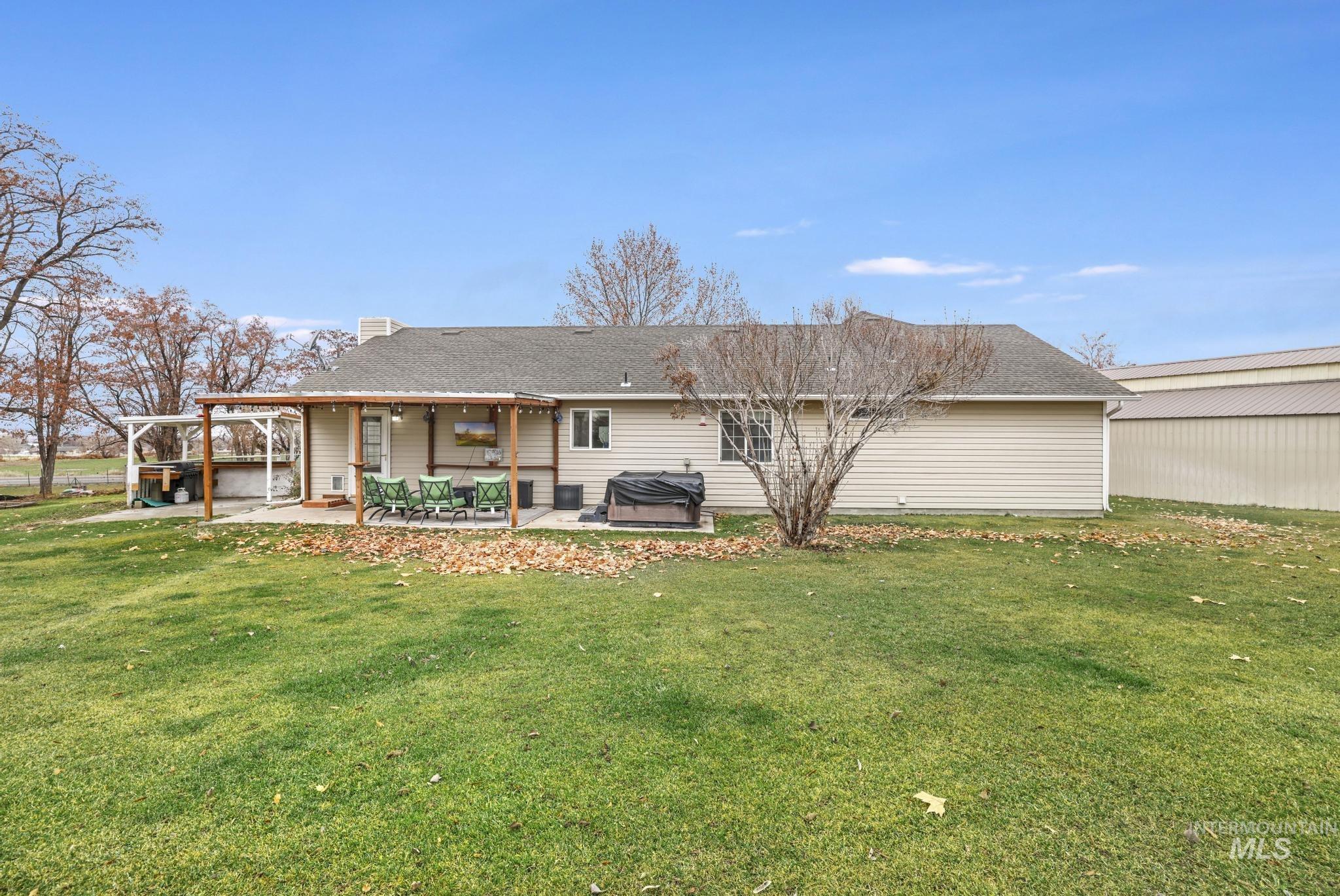 Back of house featuring a lawn, a hot tub, a patio area, a chimney, and roof with shingles