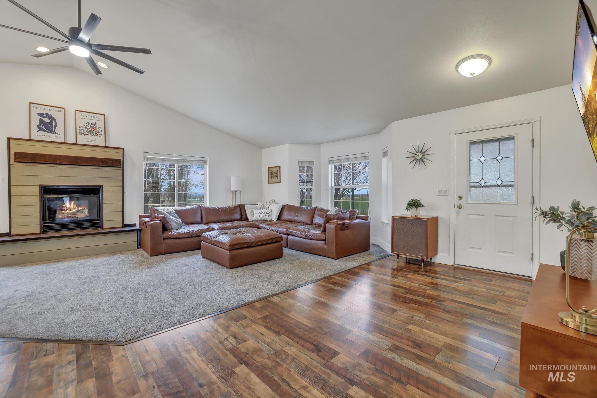 Living area featuring a glass covered fireplace, dark wood-type flooring, healthy amount of natural light, lofted ceiling, and a ceiling fan