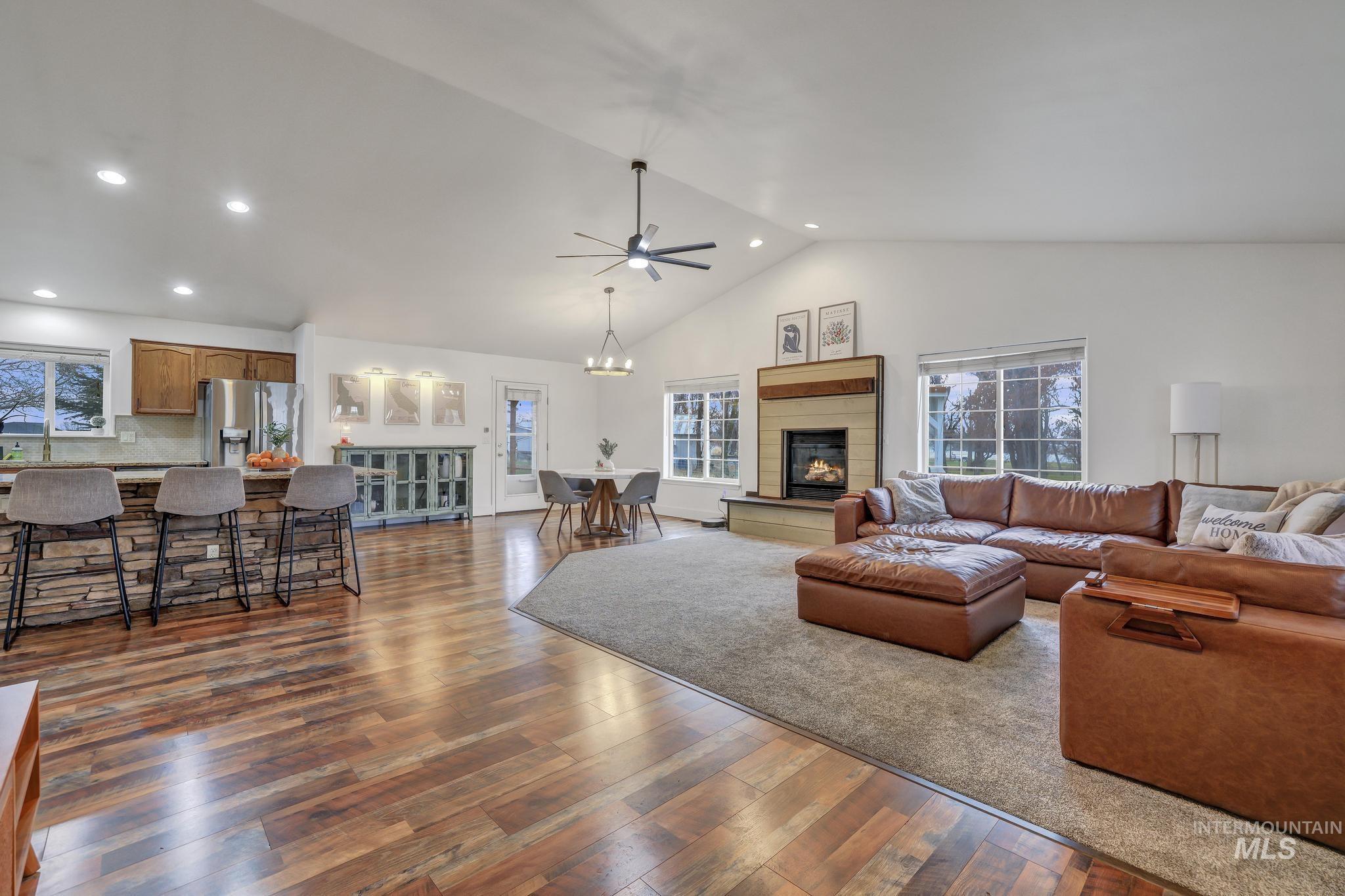 Living room featuring recessed lighting, dark wood-style floors, high vaulted ceiling, a glass covered fireplace, and a ceiling fan
