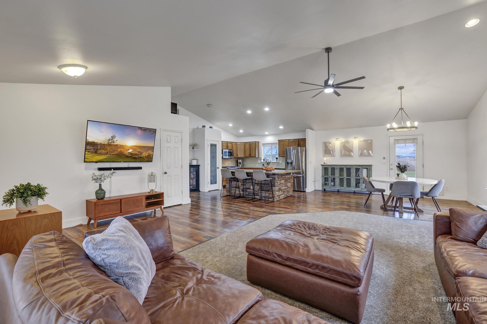 Living room featuring vaulted ceiling, ceiling fan, dark wood-style floors, recessed lighting, and a chandelier
