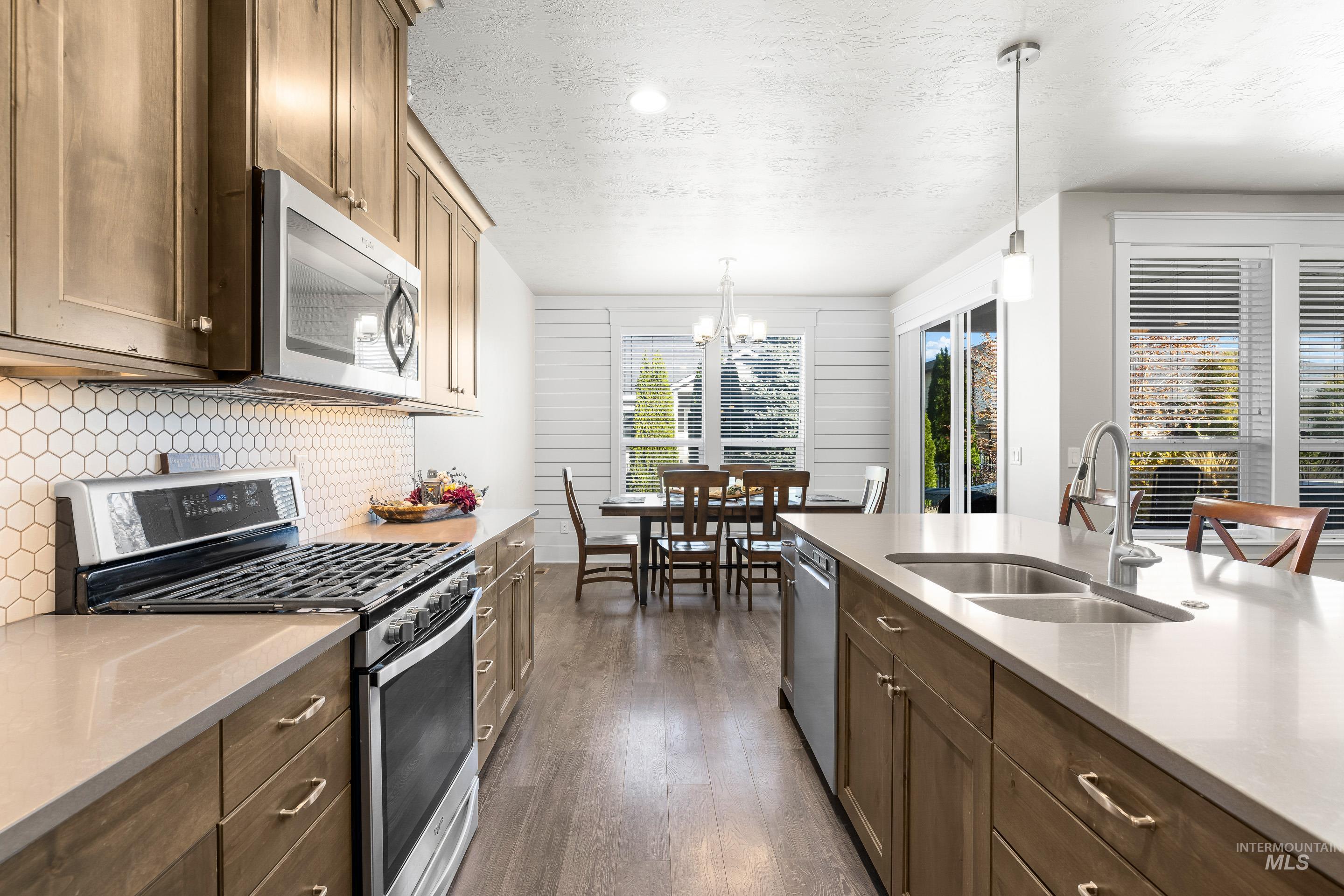 Kitchen with appliances with stainless steel finishes, light stone counters, dark wood finished floors, pendant lighting, and a chandelier