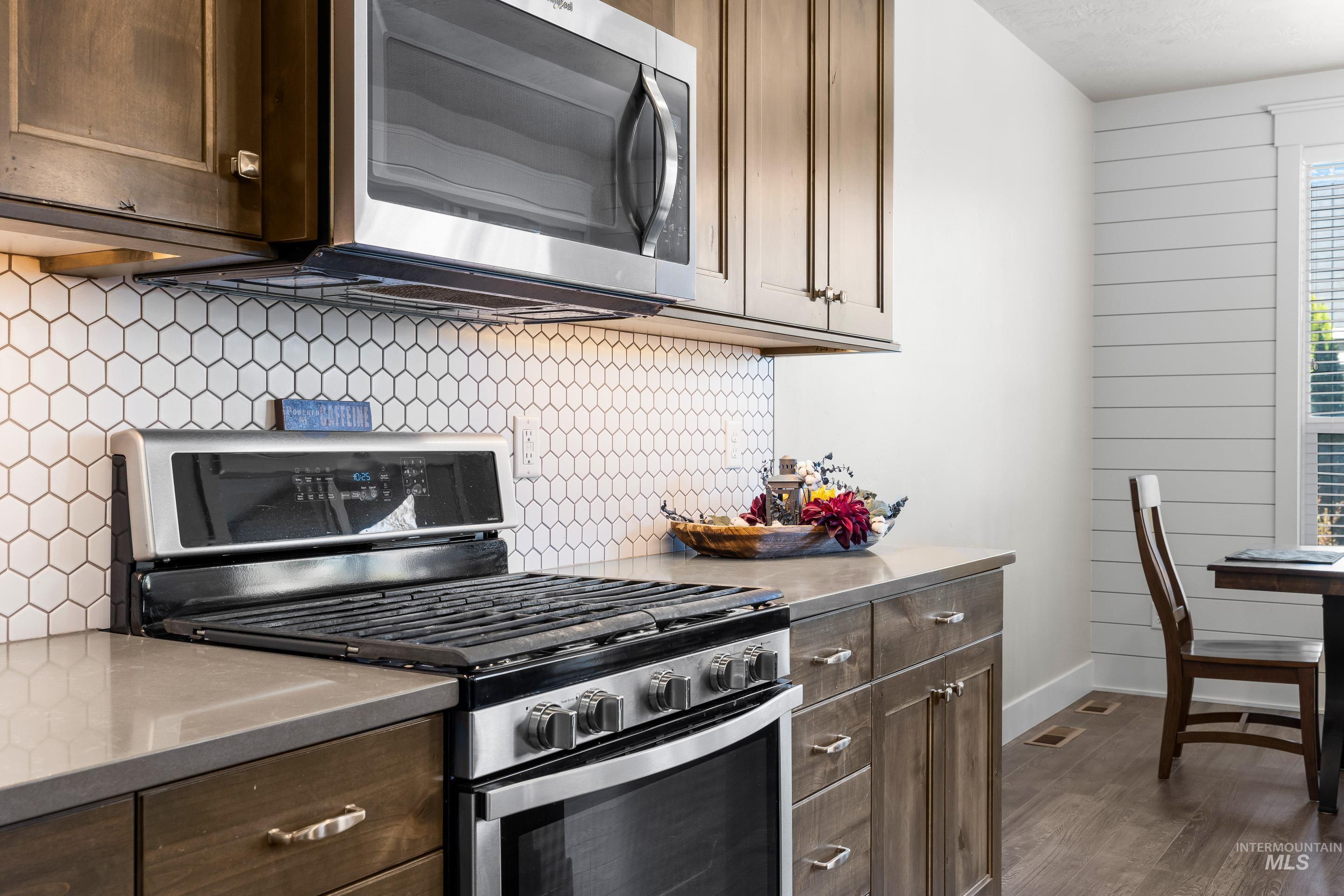Kitchen featuring stainless steel appliances, dark brown cabinets, tasteful backsplash, dark wood-style flooring, and stainless steel counters