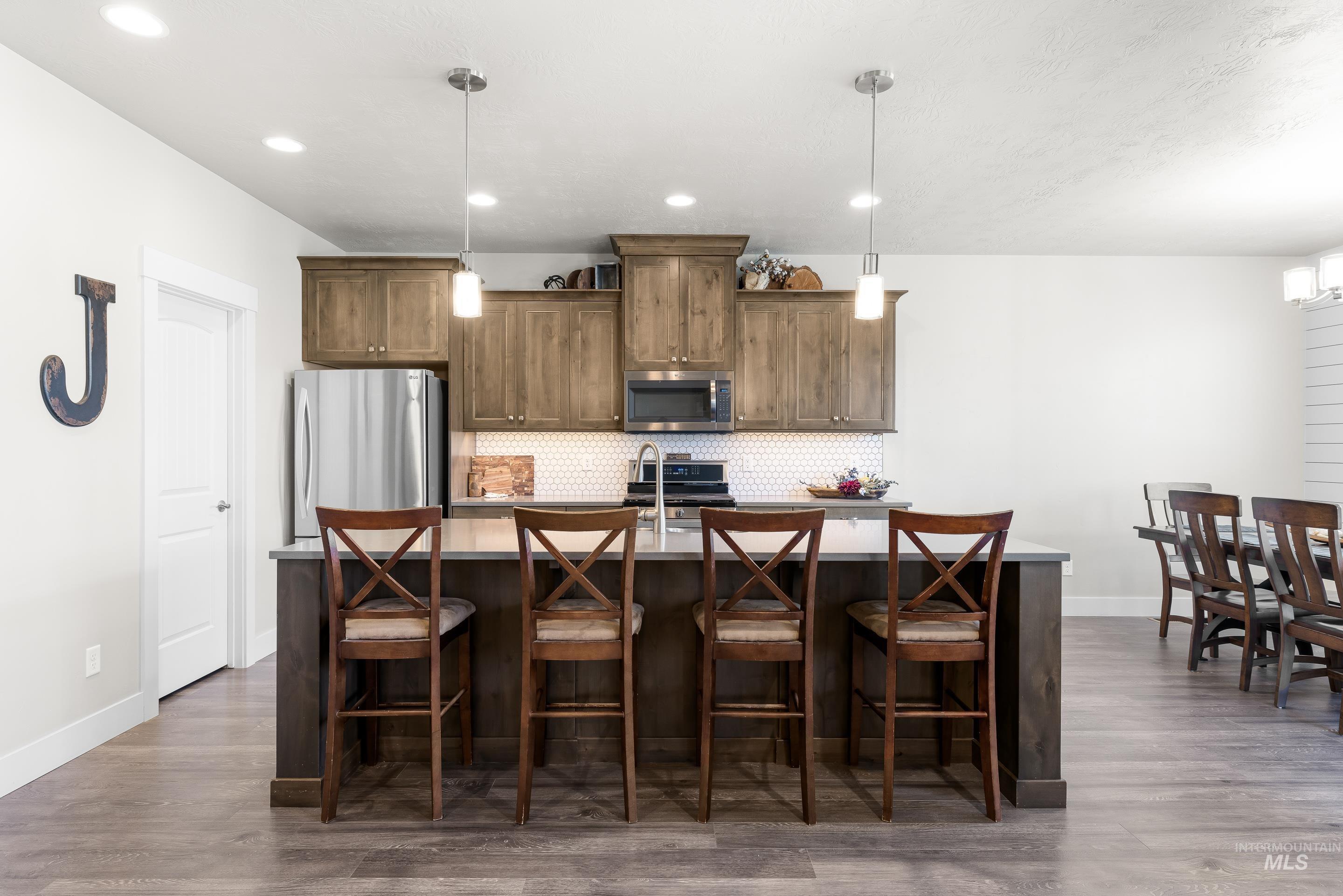 Kitchen with stainless steel appliances, a kitchen bar, decorative backsplash, decorative light fixtures, and an island with sink