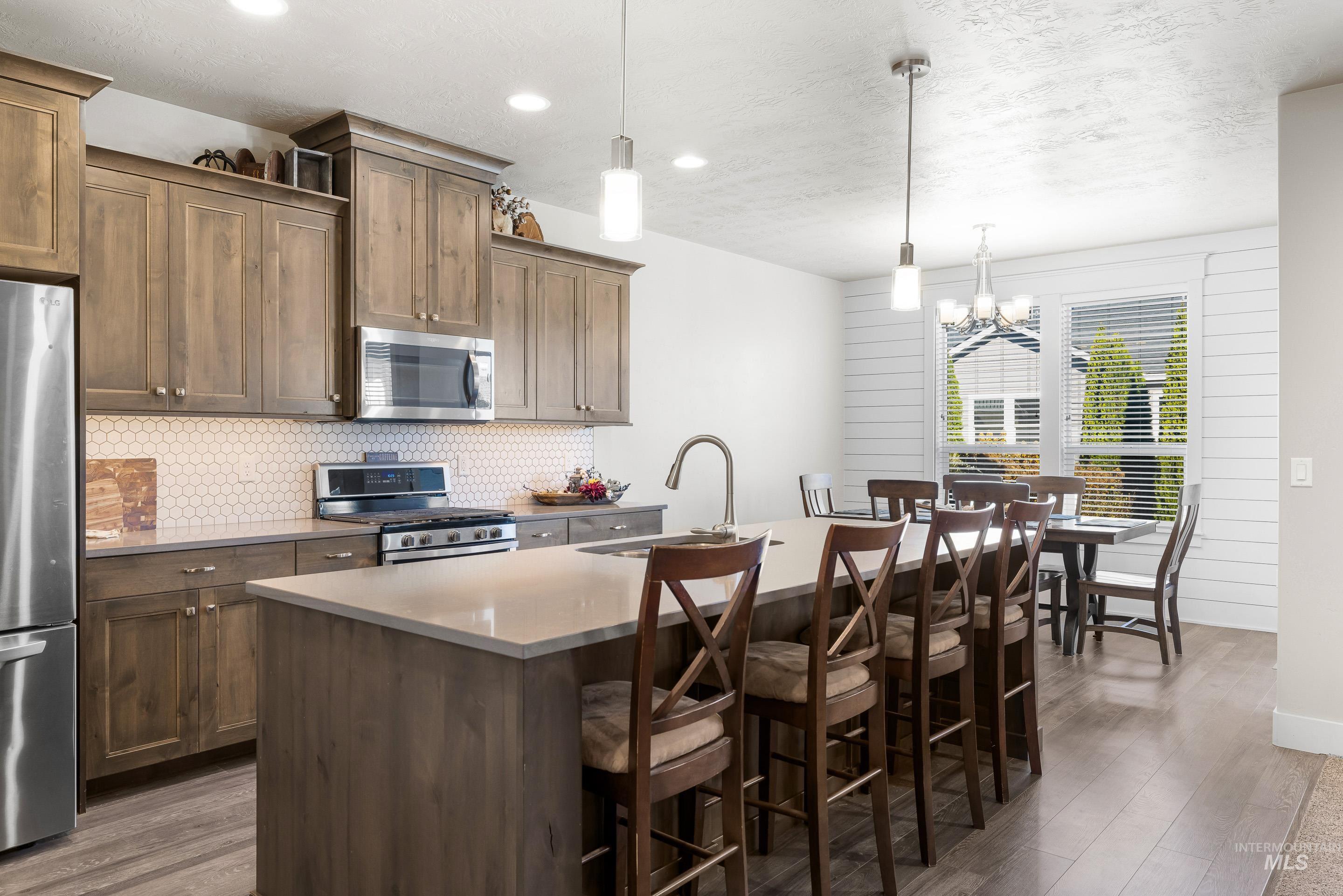Kitchen with stainless steel appliances, an island with sink, dark wood-type flooring, a kitchen breakfast bar, and a textured ceiling