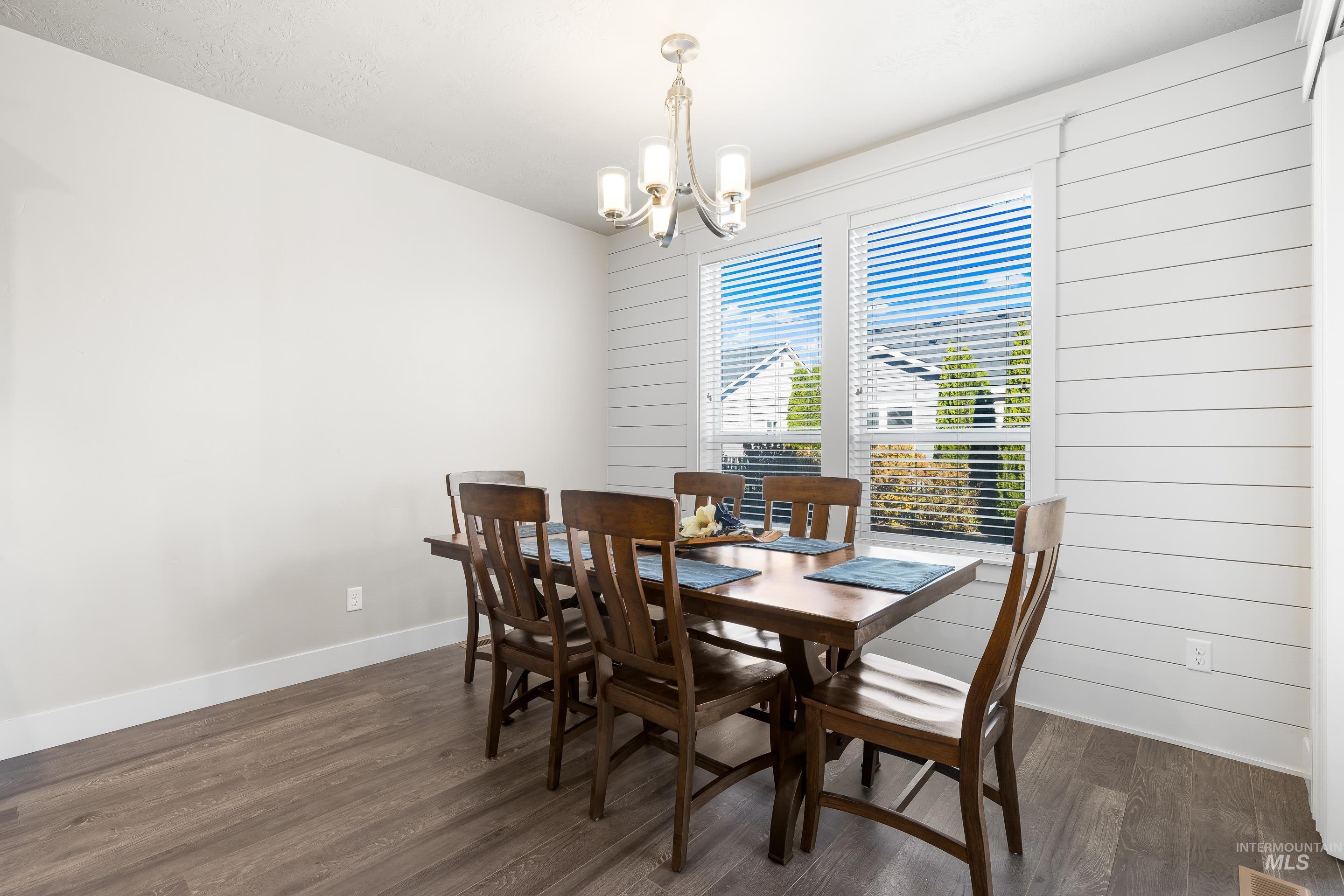 Dining room featuring dark wood-style flooring, a chandelier, and wood walls