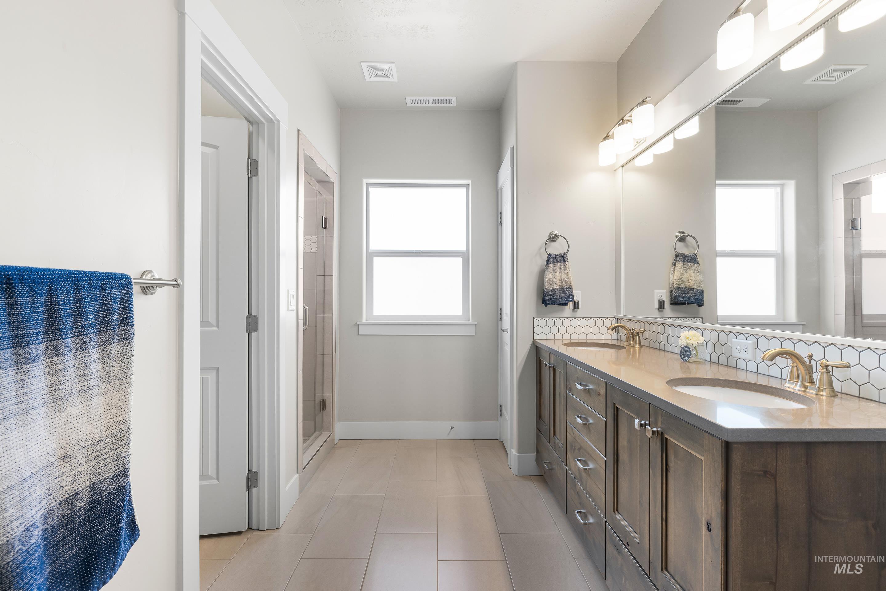 Full bath featuring double vanity, plenty of natural light, light tile patterned floors, and a stall shower