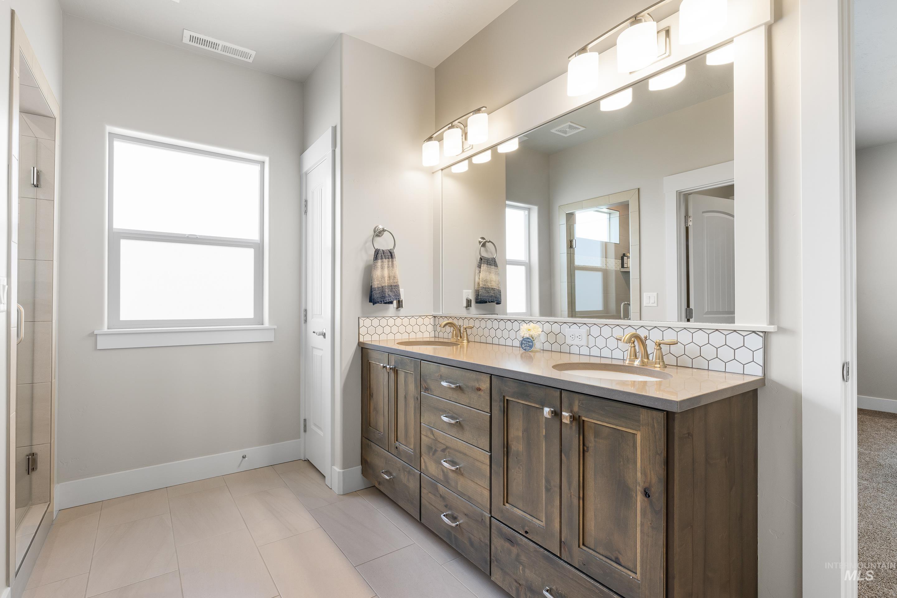 Full bathroom featuring double vanity, decorative backsplash, a tile shower, and light tile patterned flooring