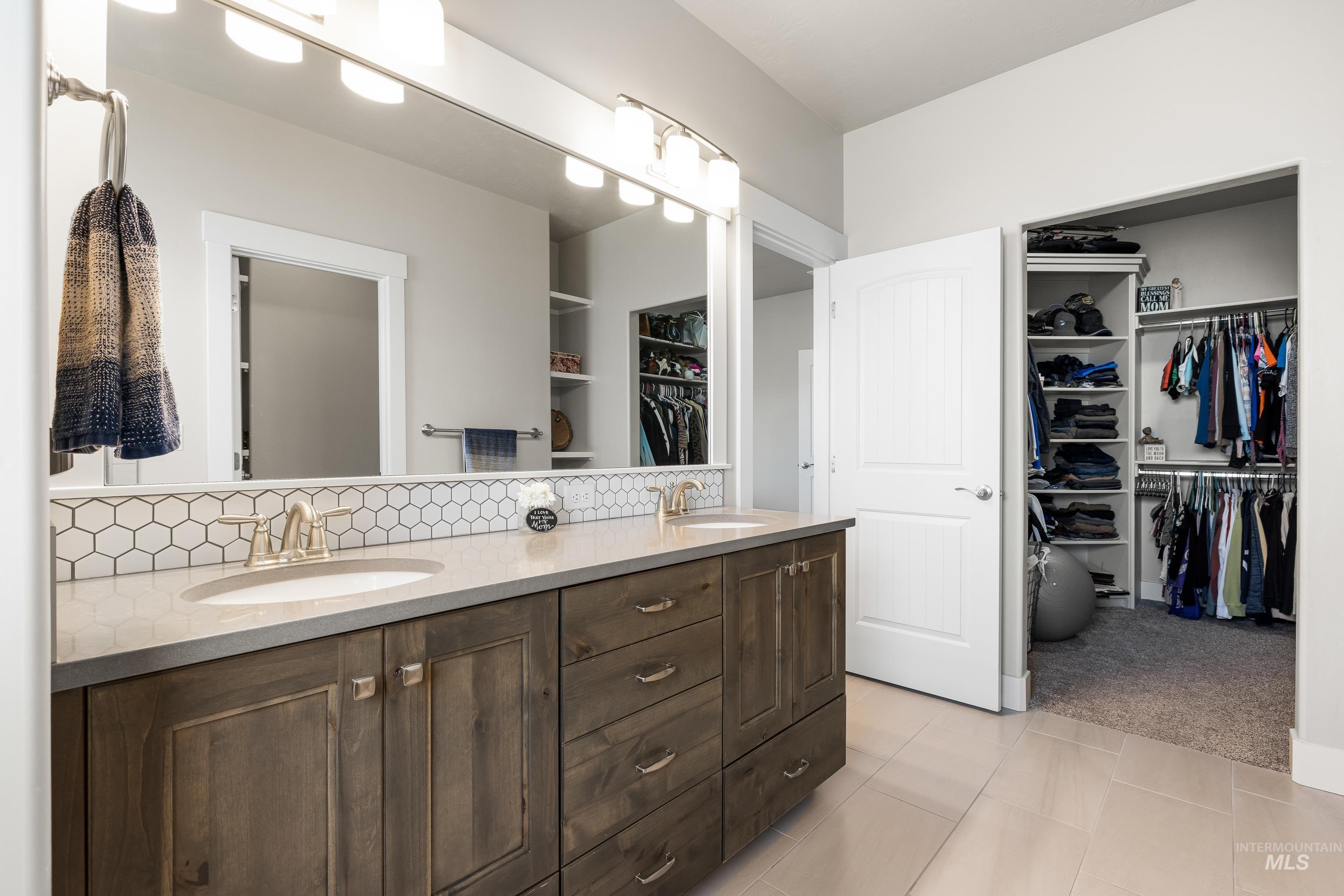 Full bath featuring a walk in closet, double vanity, light tile patterned floors, and light carpet