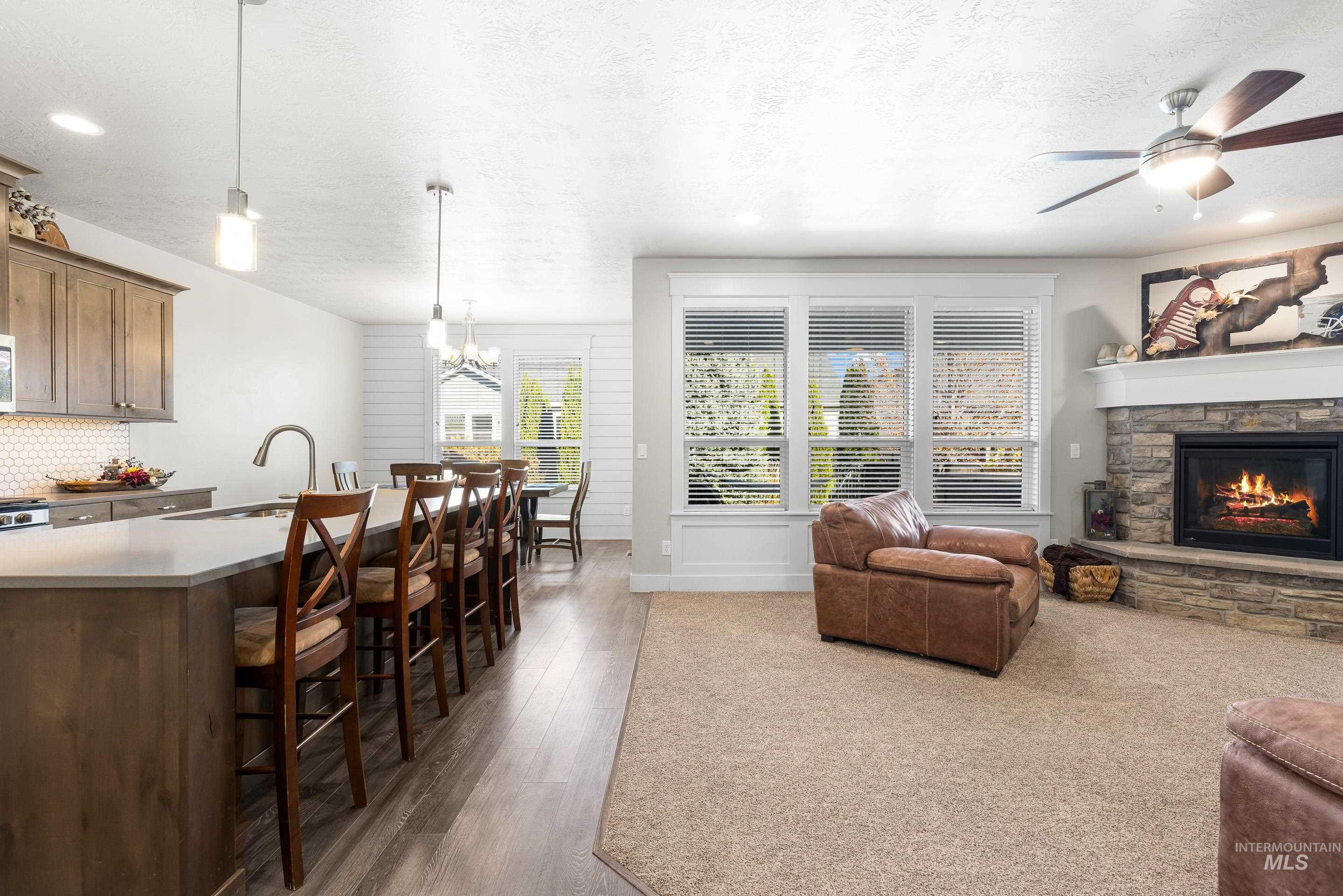 Living room with a textured ceiling, a ceiling fan, dark wood-type flooring, a fireplace, and a chandelier