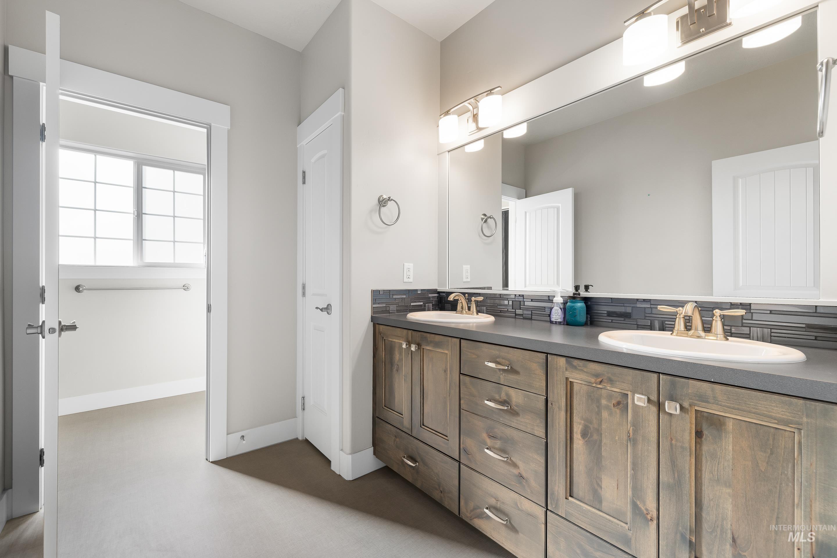 Full bath with finished concrete floors, double vanity, and backsplash