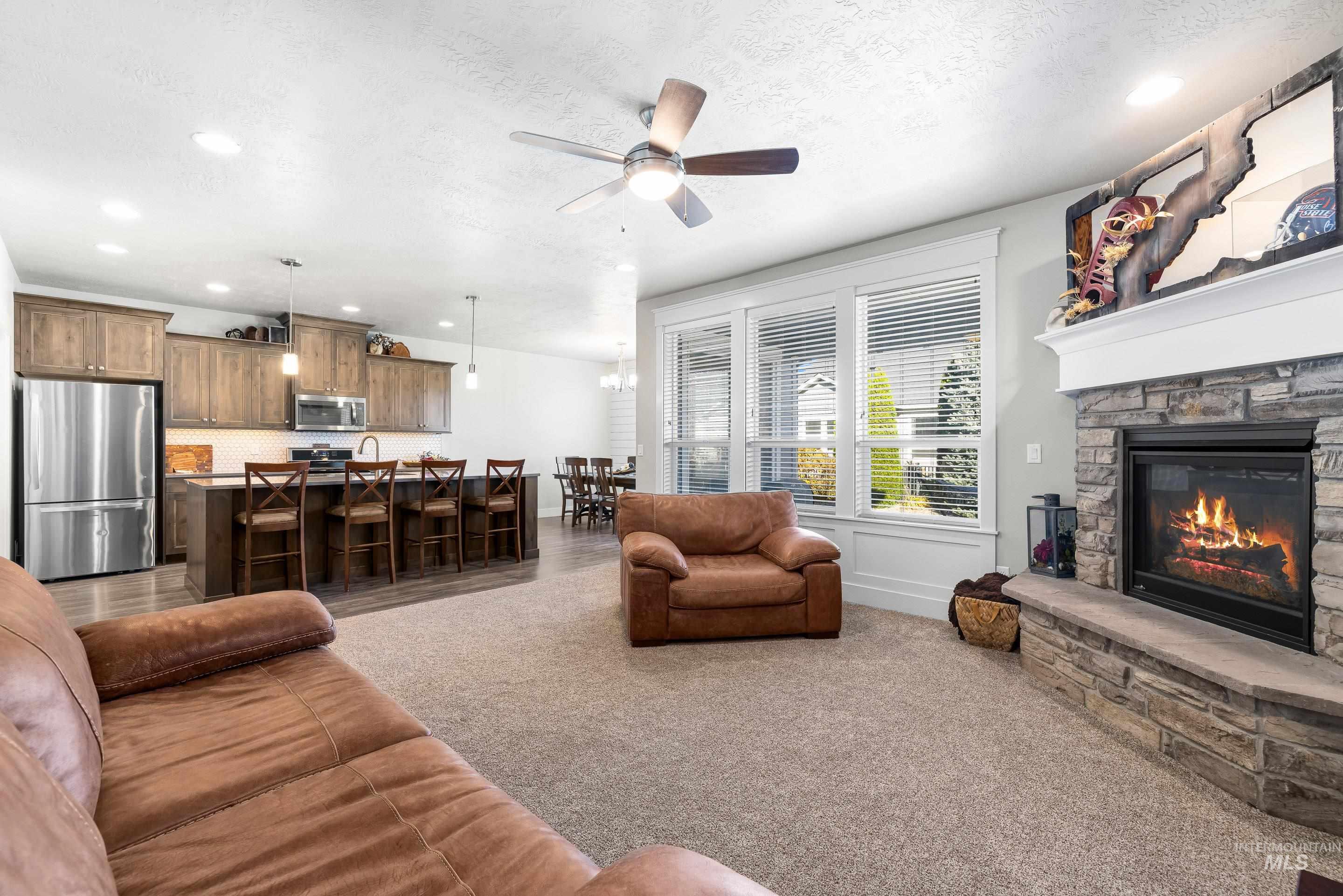Carpeted living room with a ceiling fan, a stone fireplace, recessed lighting, and a textured ceiling
