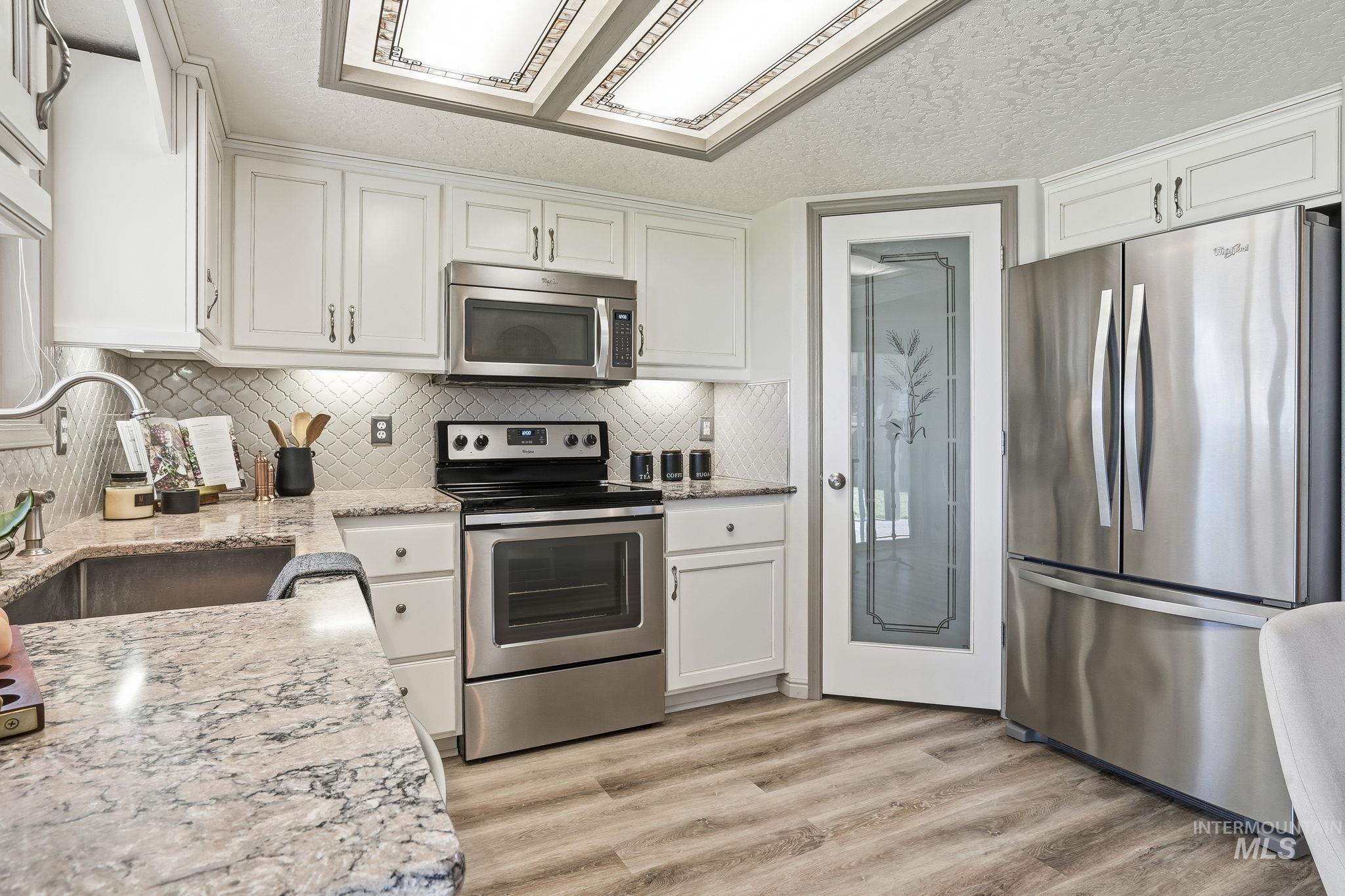 Kitchen with stainless steel appliances, white cabinetry, a textured ceiling, light stone counters, and light wood-style flooring
