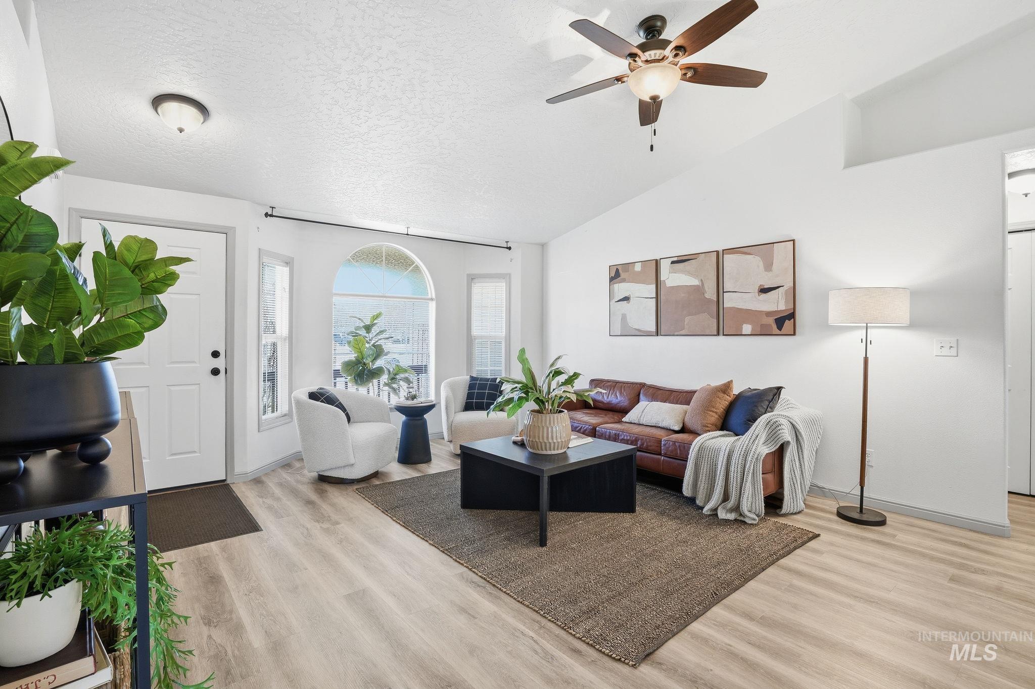 Living area with a textured ceiling, light wood finished floors, lofted ceiling, and ceiling fan
