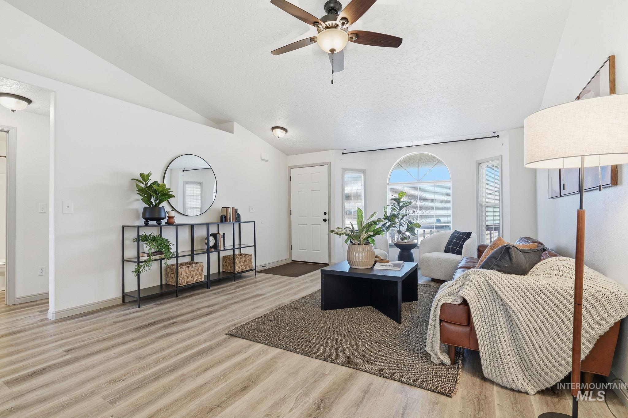 Living room featuring lofted ceiling, light wood-style floors, a ceiling fan, and a textured ceiling