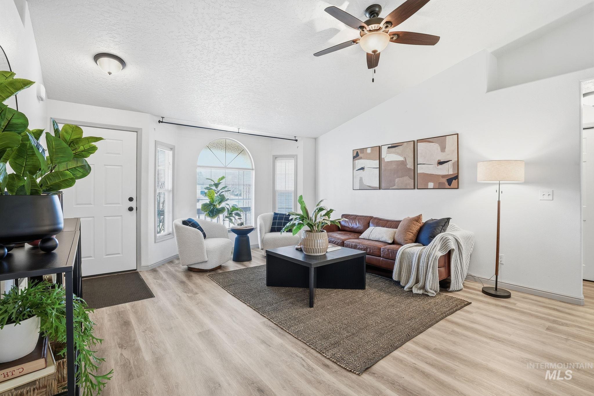 Living area with a textured ceiling, light wood-type flooring, vaulted ceiling, and ceiling fan